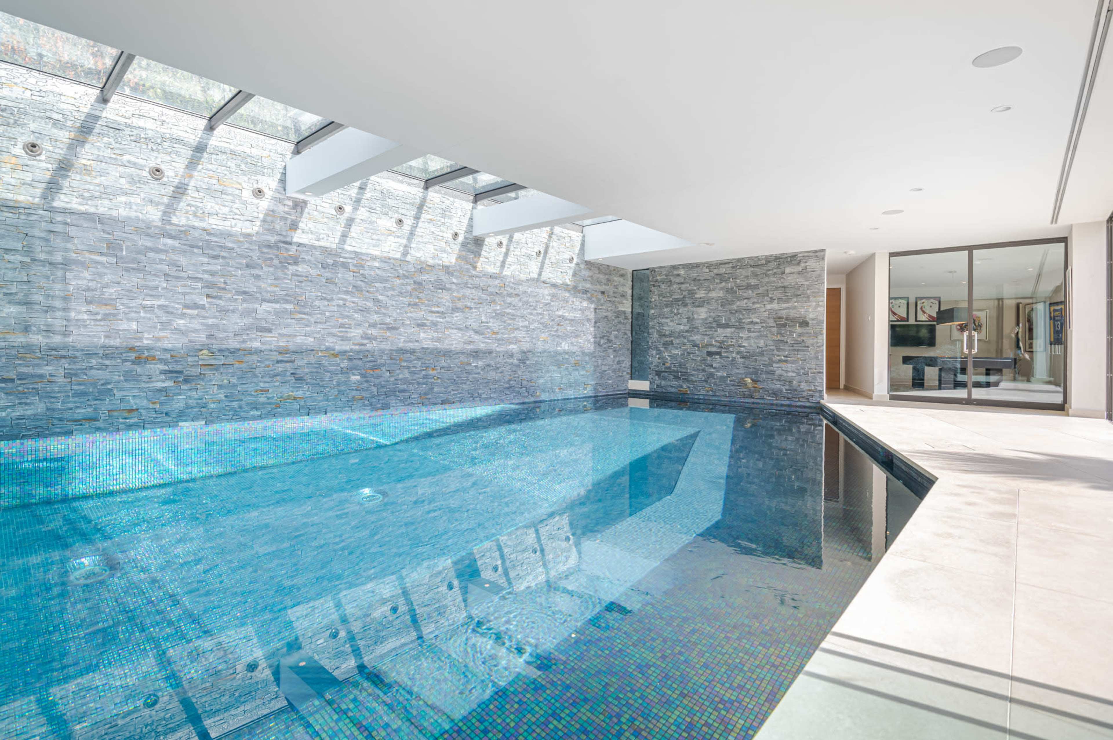 An indoor swimming pool surrounded by stone walls and large windows that allow natural light to enter.