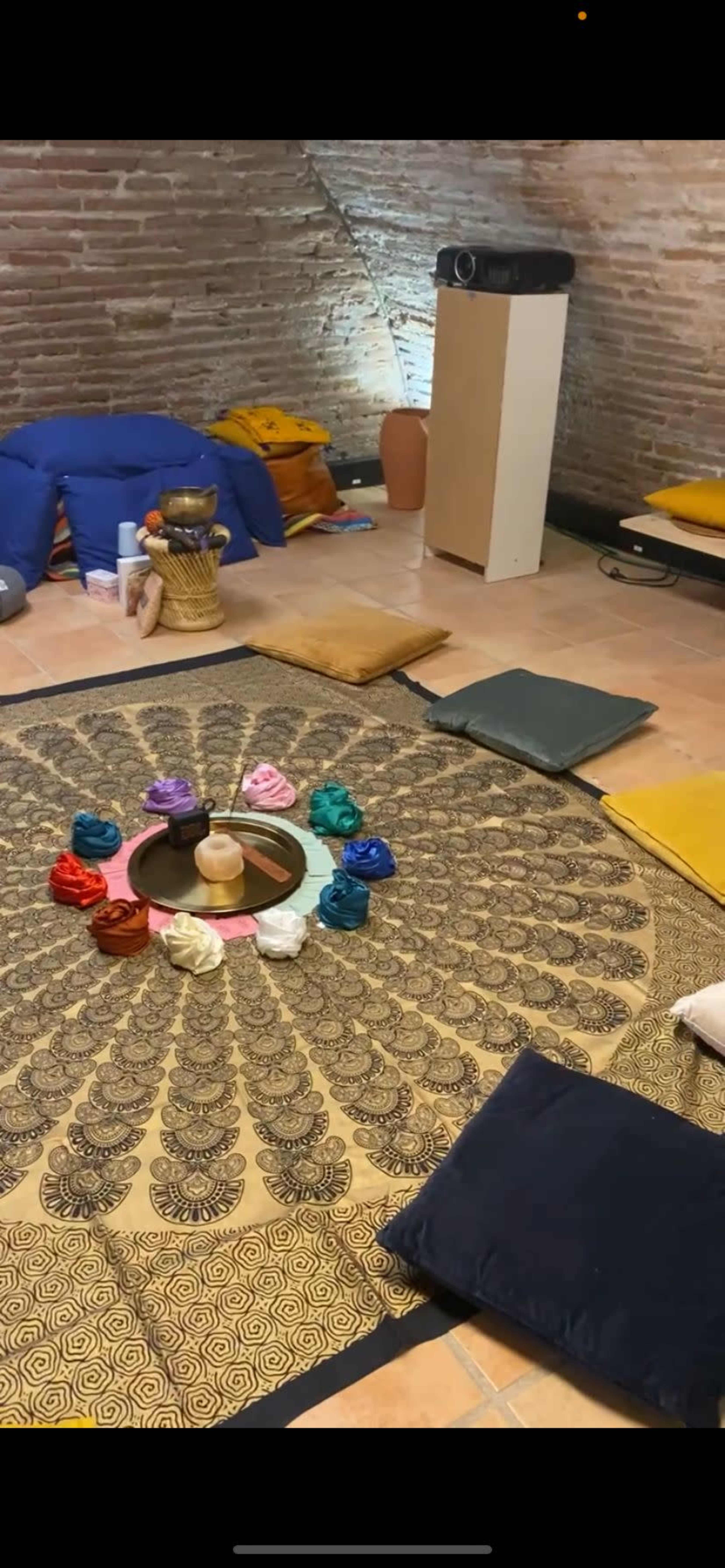 The scene shows a dimly lit room with various cushions arranged around a central circular display on a patterned mat.