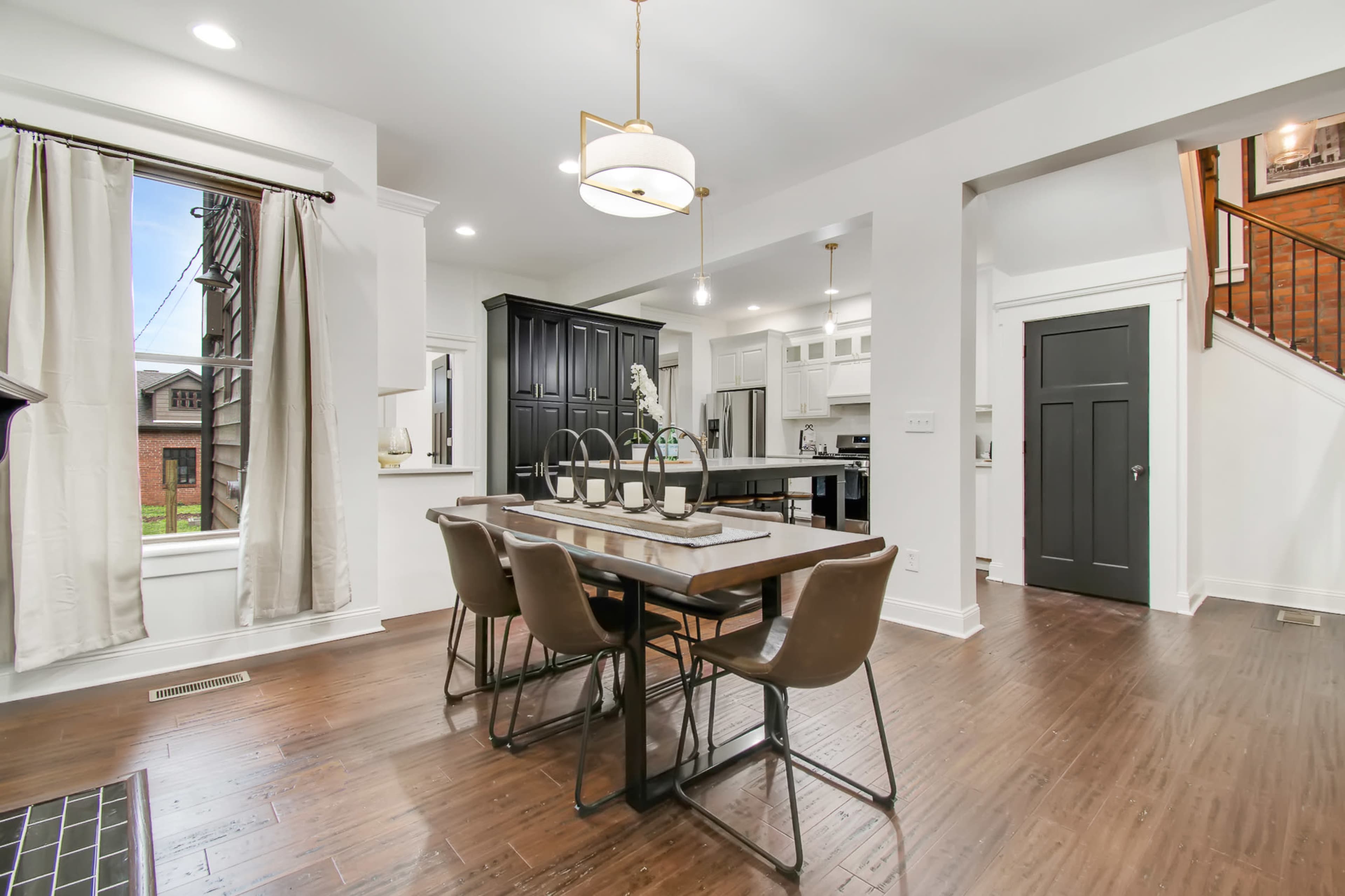 A modern dining area with a table set for six, surrounded by chairs, and a view of the kitchen and an entrance hallway.