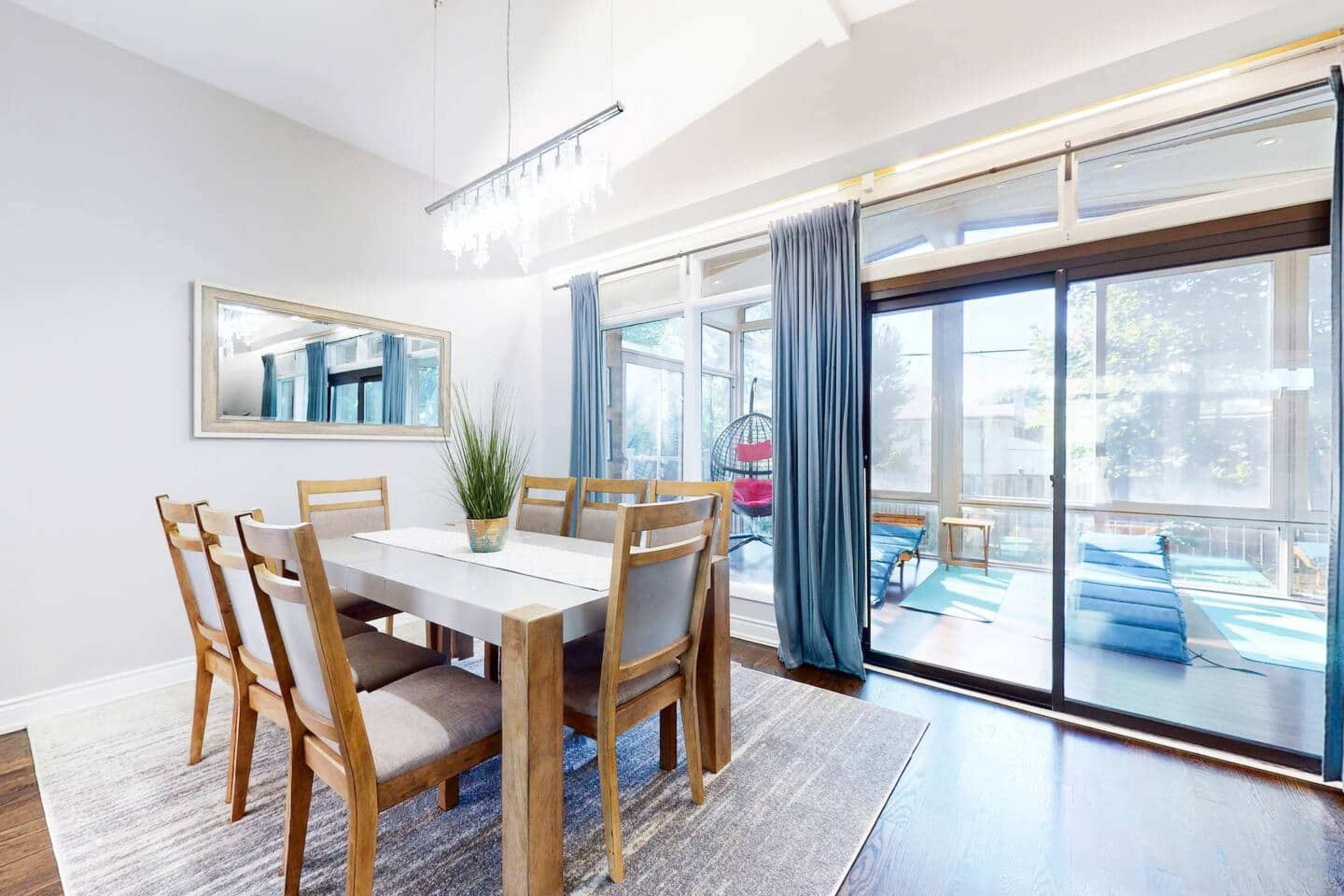 A modern dining area features a wooden table with six chairs, a large mirror, and glass doors that lead to a patio with lounge chairs.