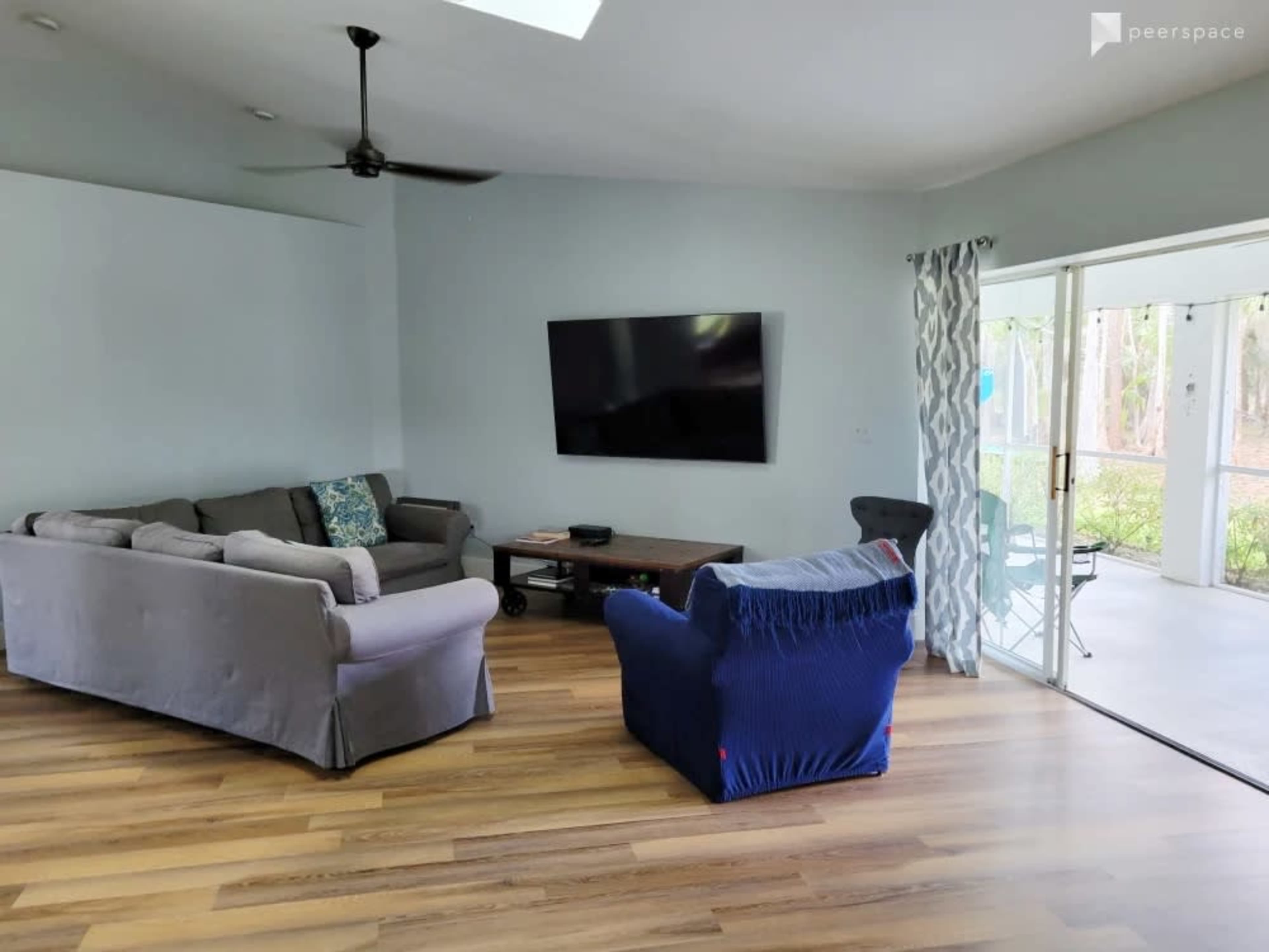 The room features two sofas, a television mounted on the wall, and a sliding glass door leading to a patio area.