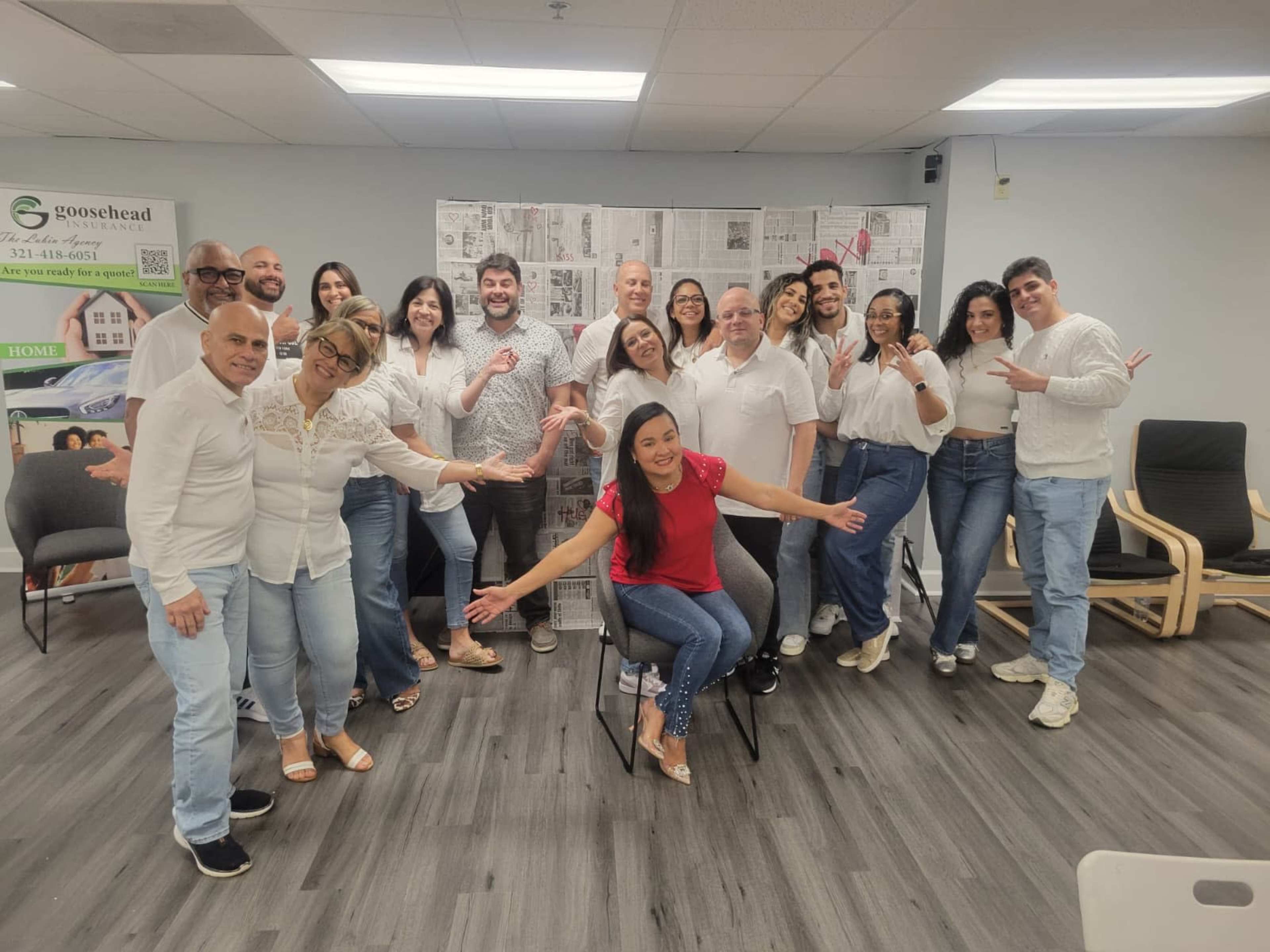 A group of people in casual attire poses together in a bright office setting.