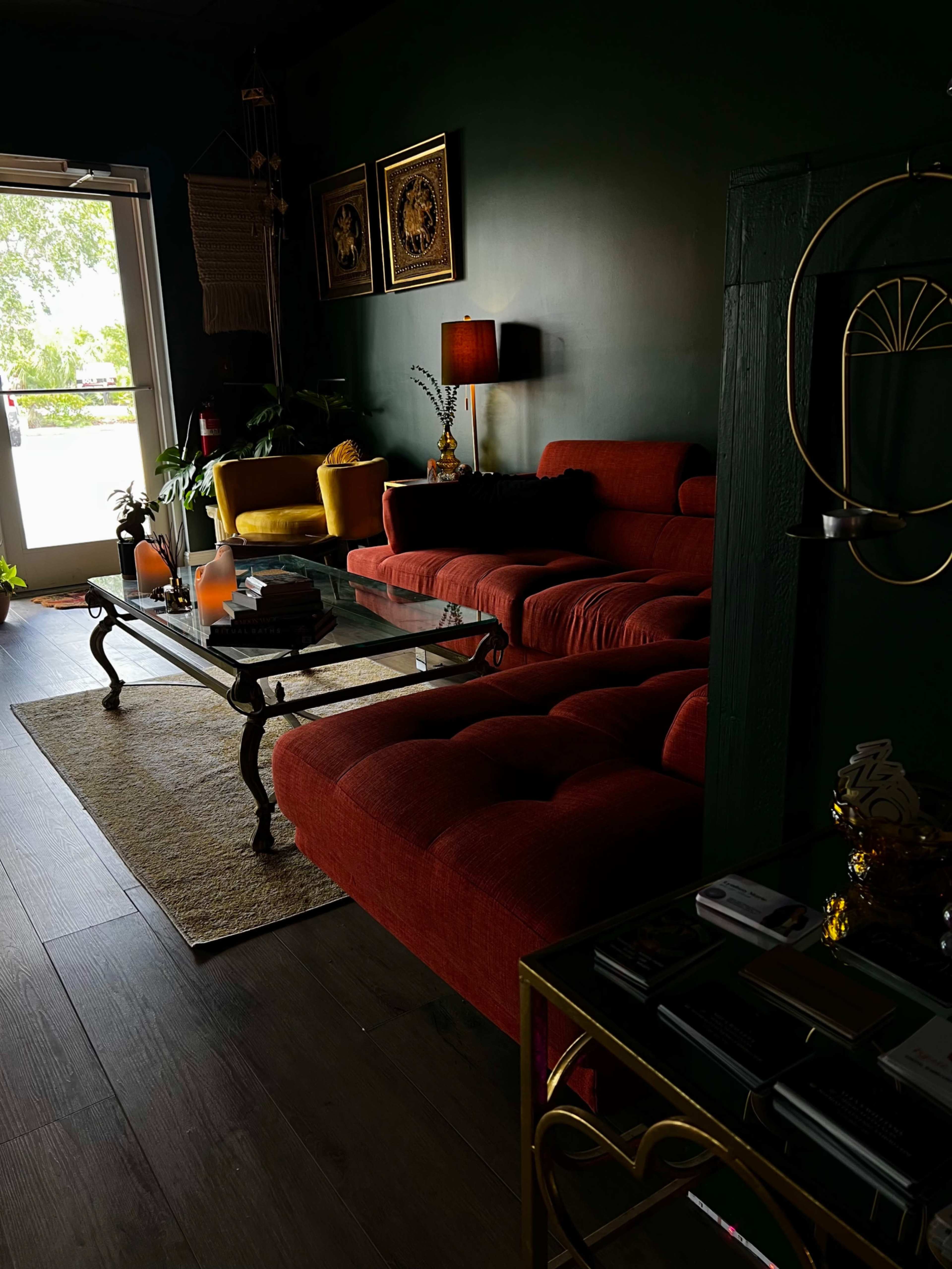 A dark green living room features a red sectional sofa, a glass coffee table, and decorative plants near the entrance.