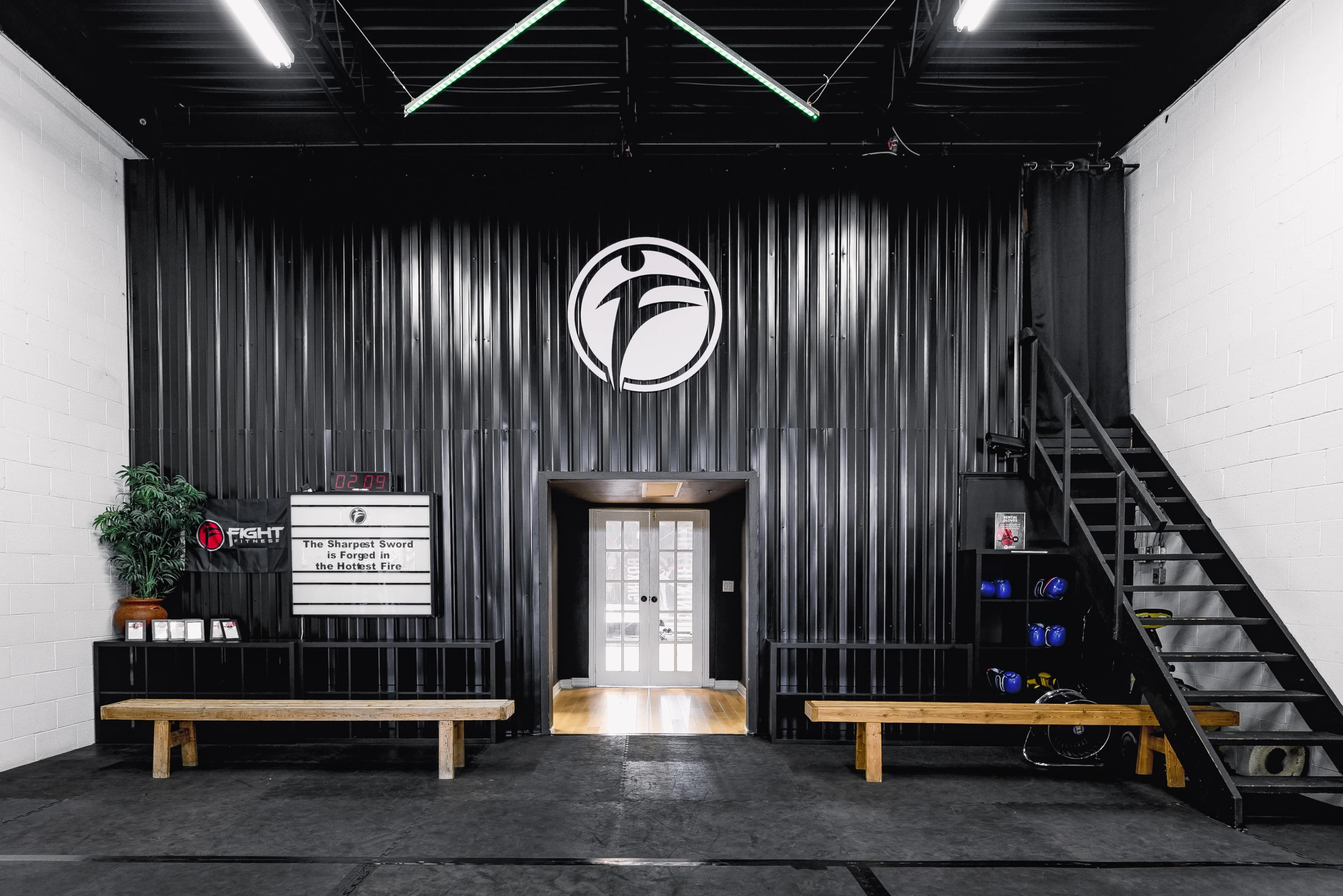 A gym entrance with black corrugated walls, benches, a staircase, and a digital clock displaying the time.