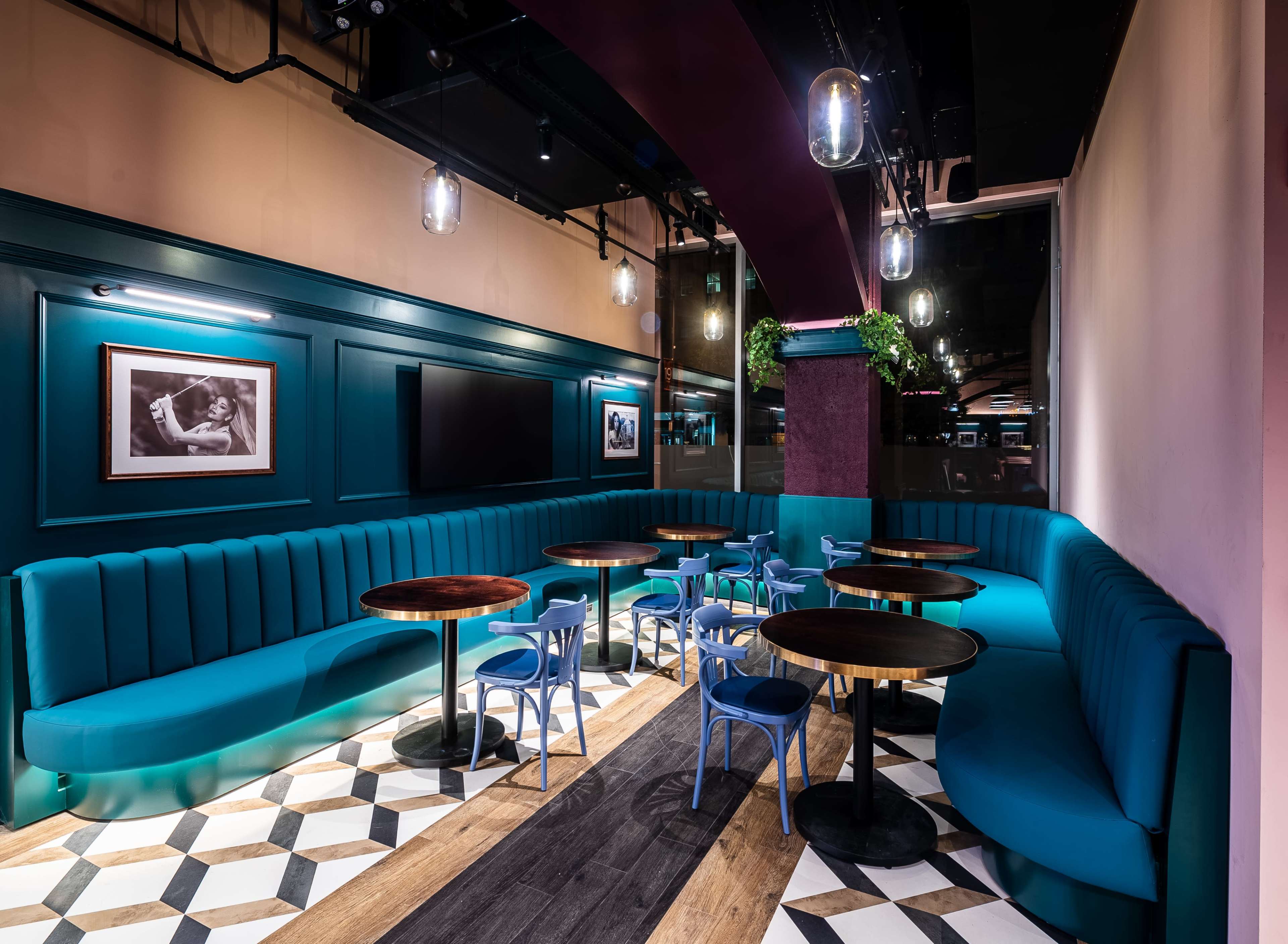 A modern café interior features teal banquette seating and wooden tables on a patterned floor, illuminated by pendant lights.