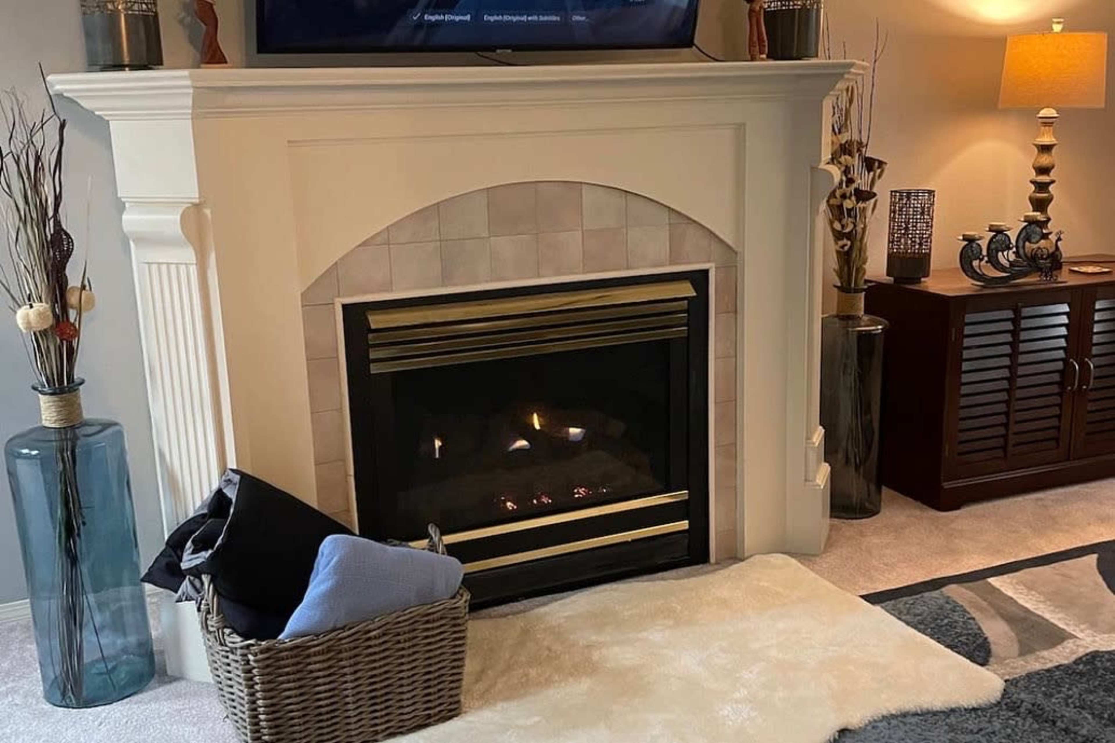 A living room with a gas fireplace, a woven basket with blankets in front, and a television mounted above the mantel.