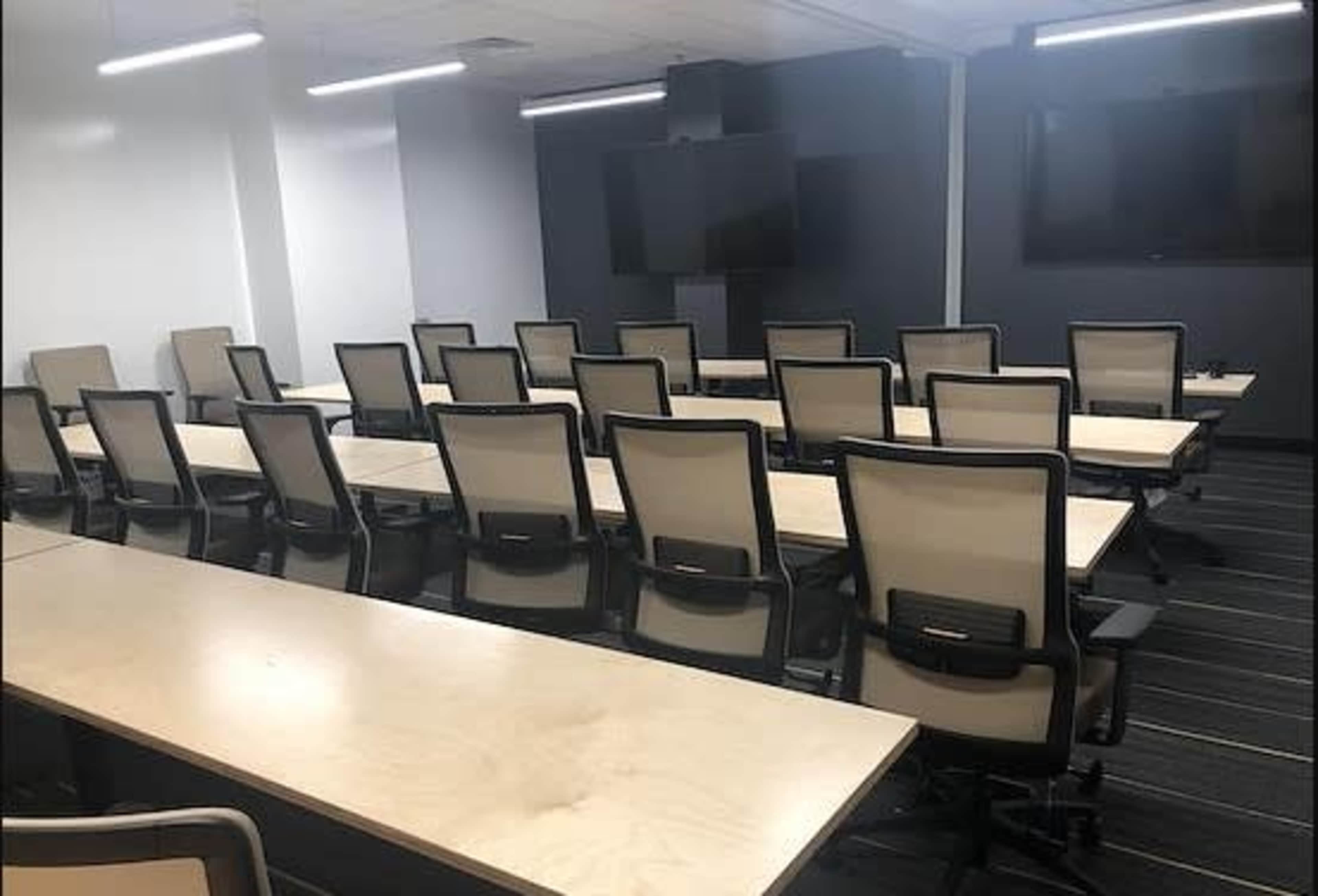 A modern conference room with rows of tables and chairs, equipped with large screens on the walls.