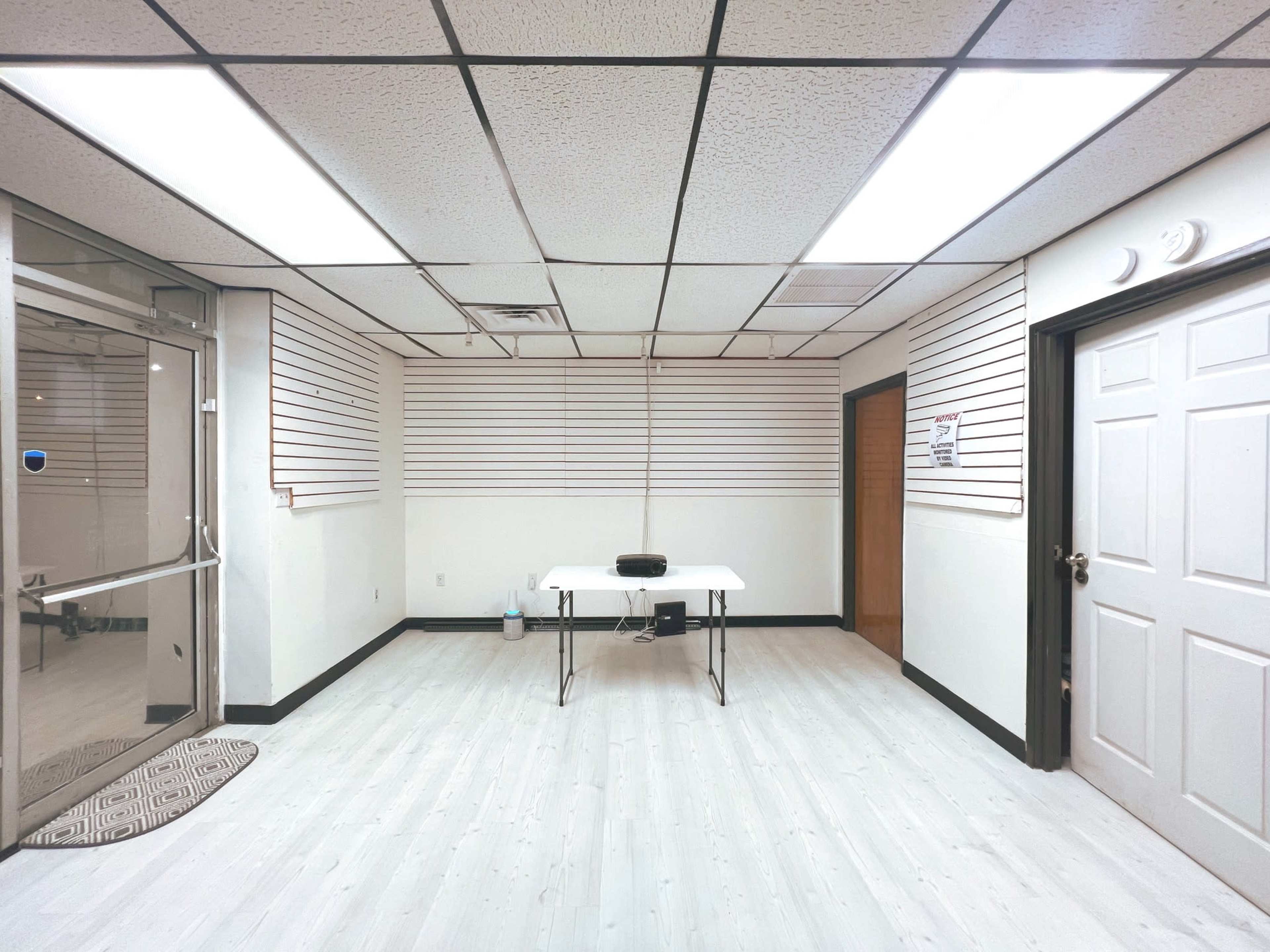 An empty room with a table in the center, white walls, and a door on the right side.