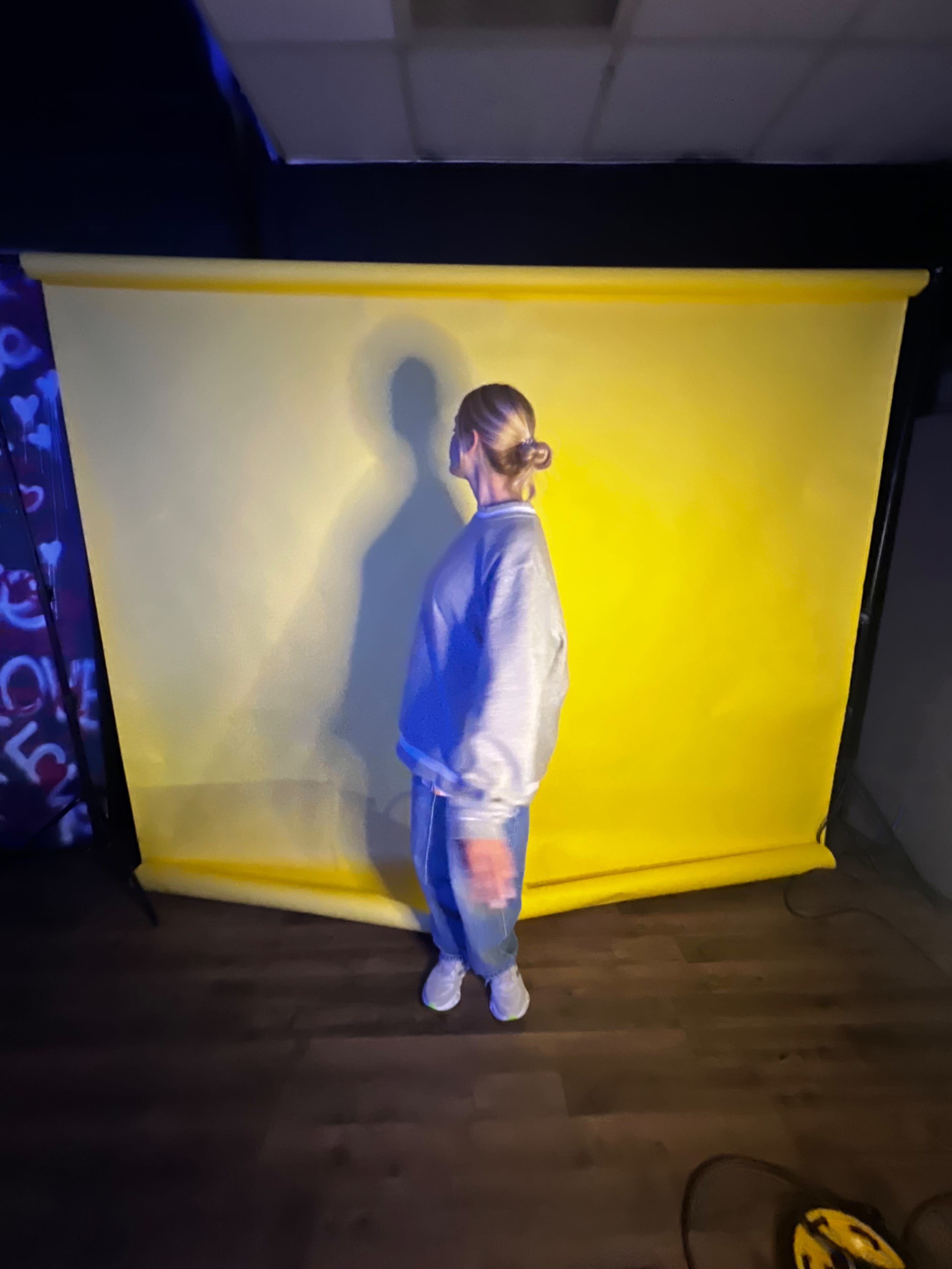 A person stands against a bright yellow backdrop with their shadow cast on the wall.