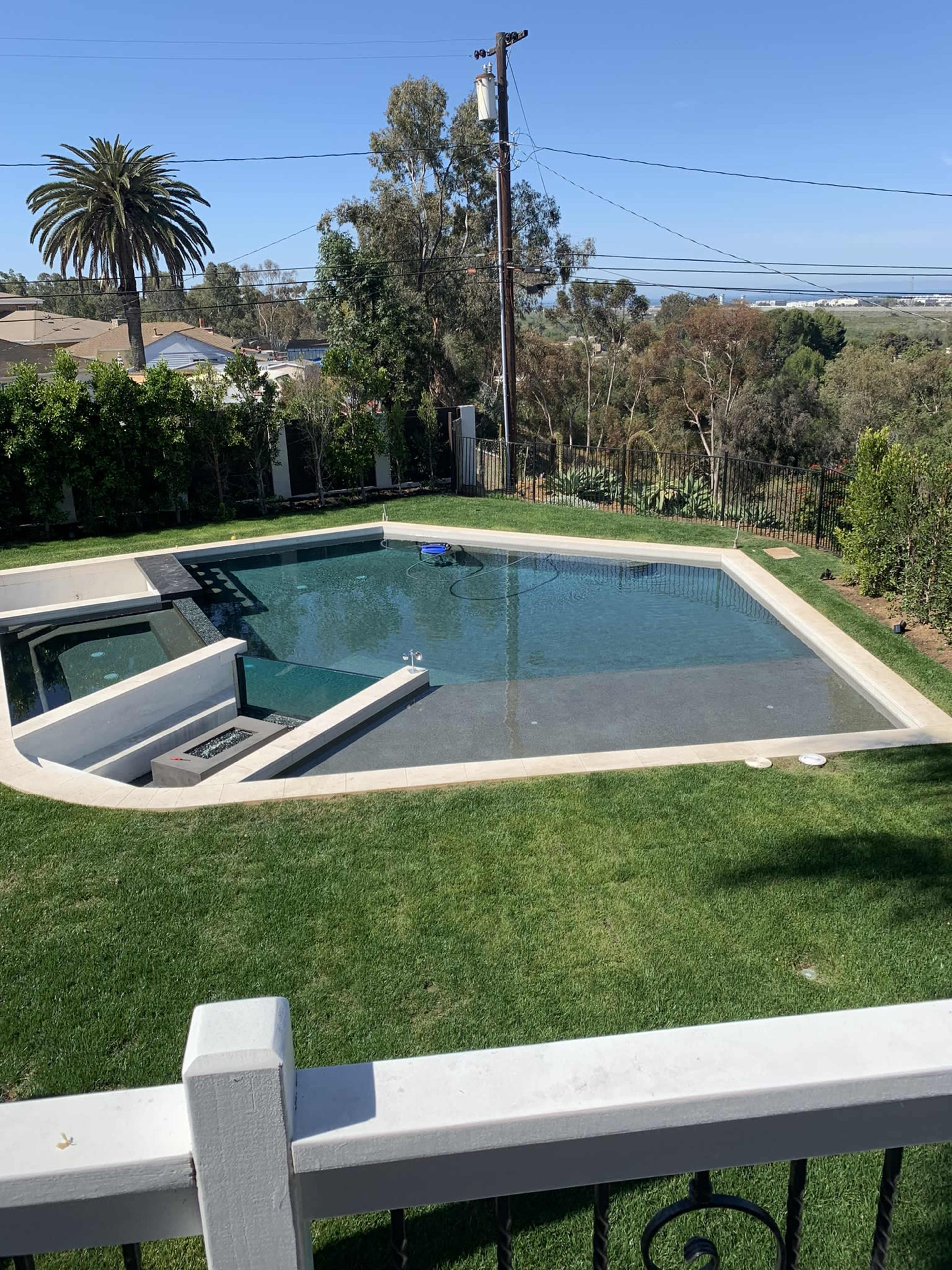 A rectangular swimming pool surrounded by a grassy area and bordered by trees and a fence.