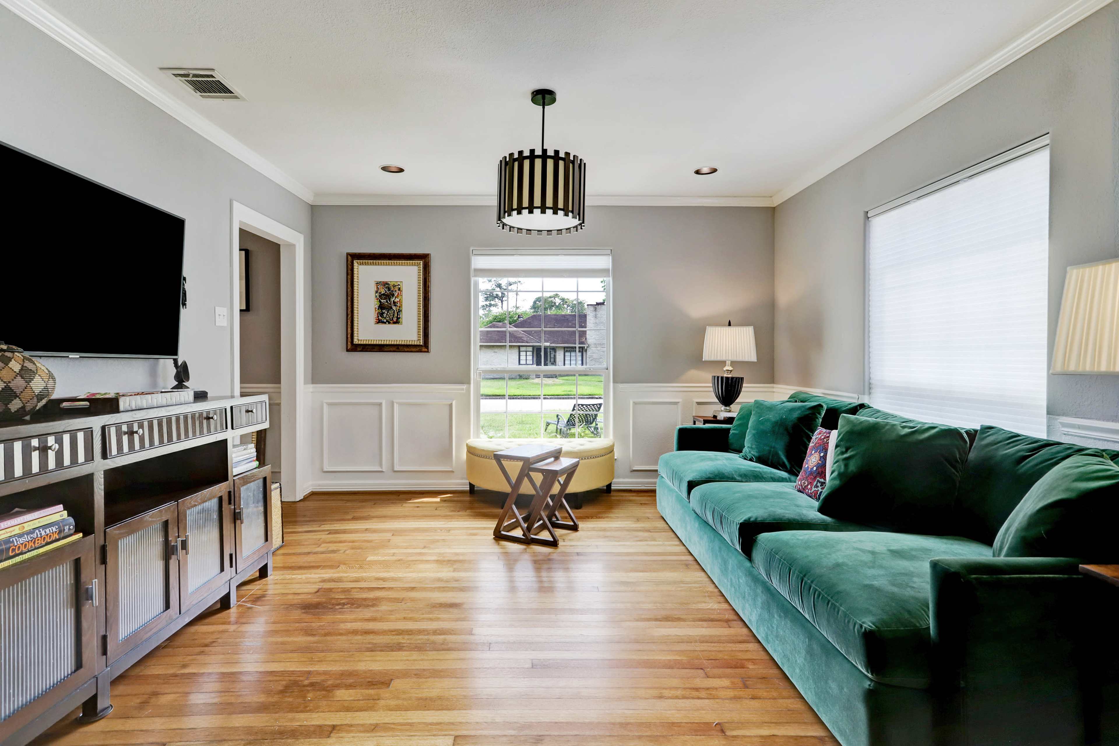 The living room features a green sofa, a television mounted on the wall, and a window with a view of the outdoors.