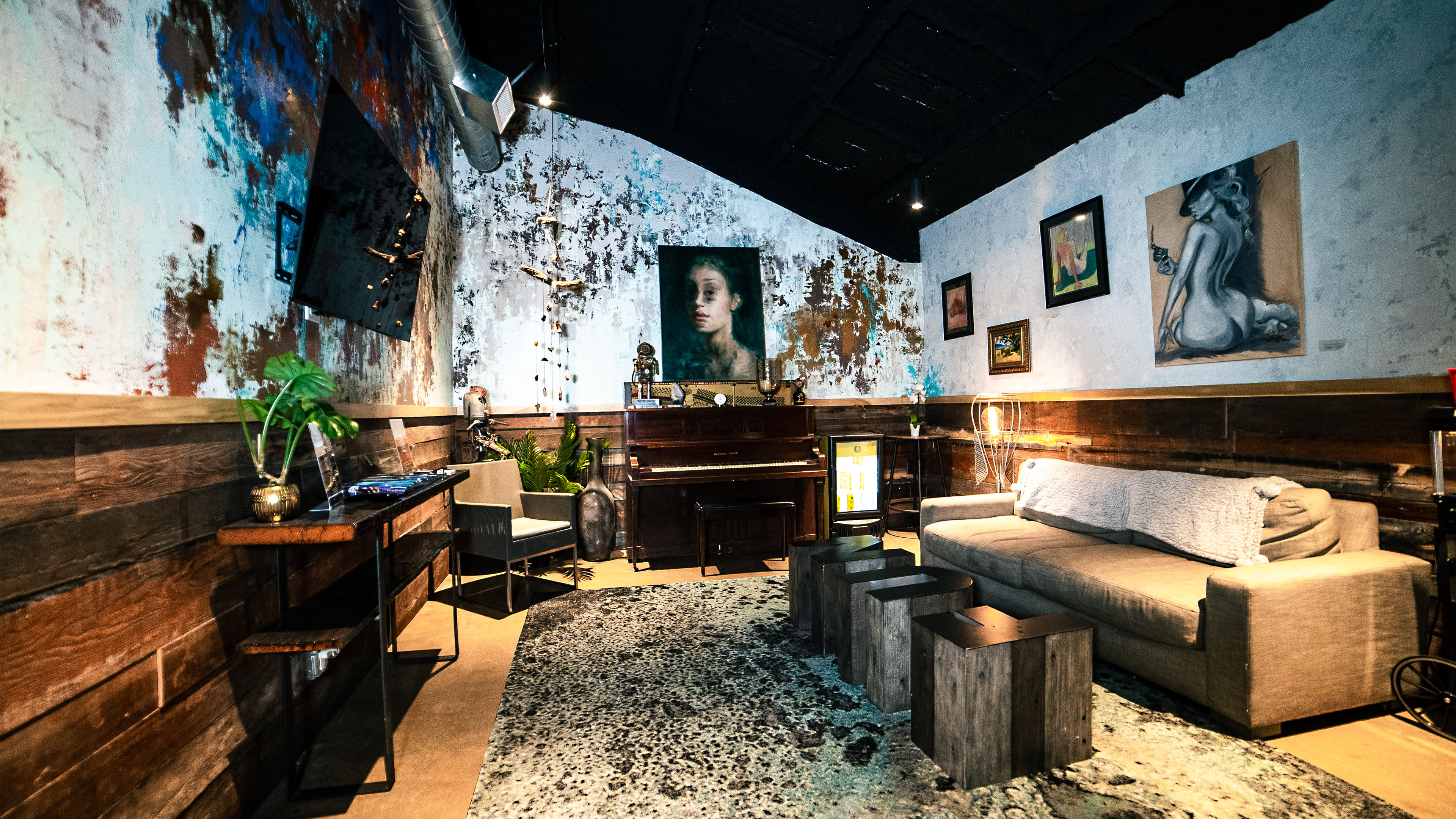 A cozy lounge area with a piano, artwork on the walls, and a sofa arranged around a textured rug.
