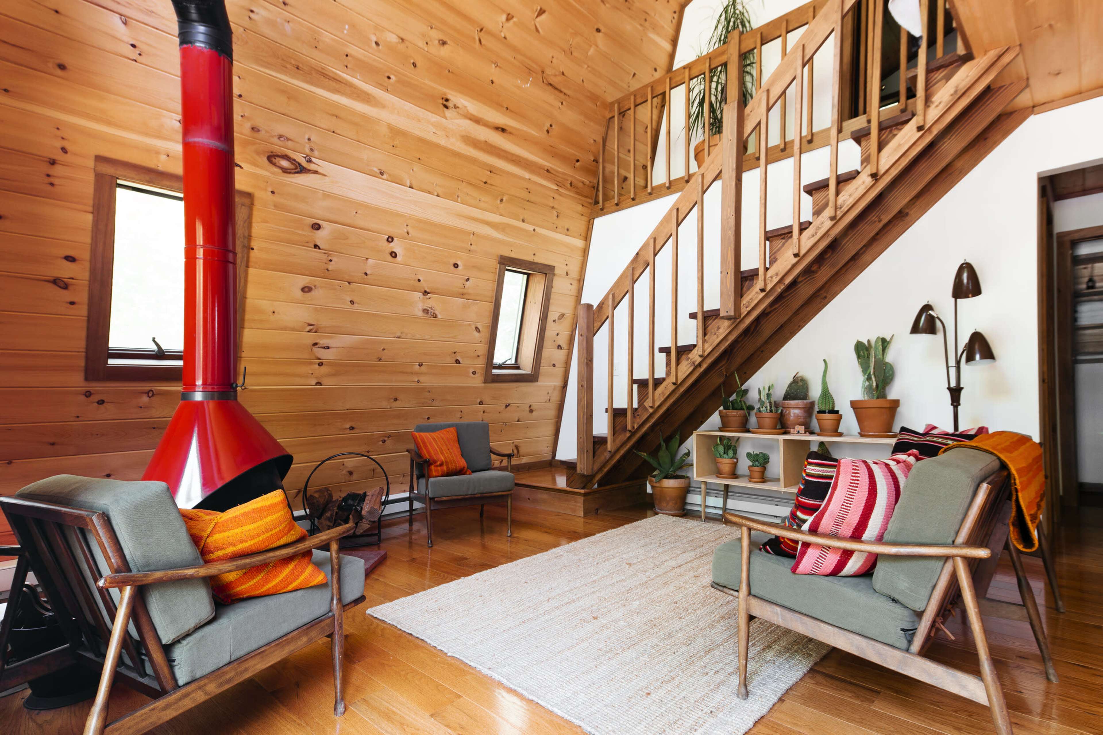A wood-paneled living area with two chairs, a red stove, and a staircase leading to an upper level, surrounded by potted plants.