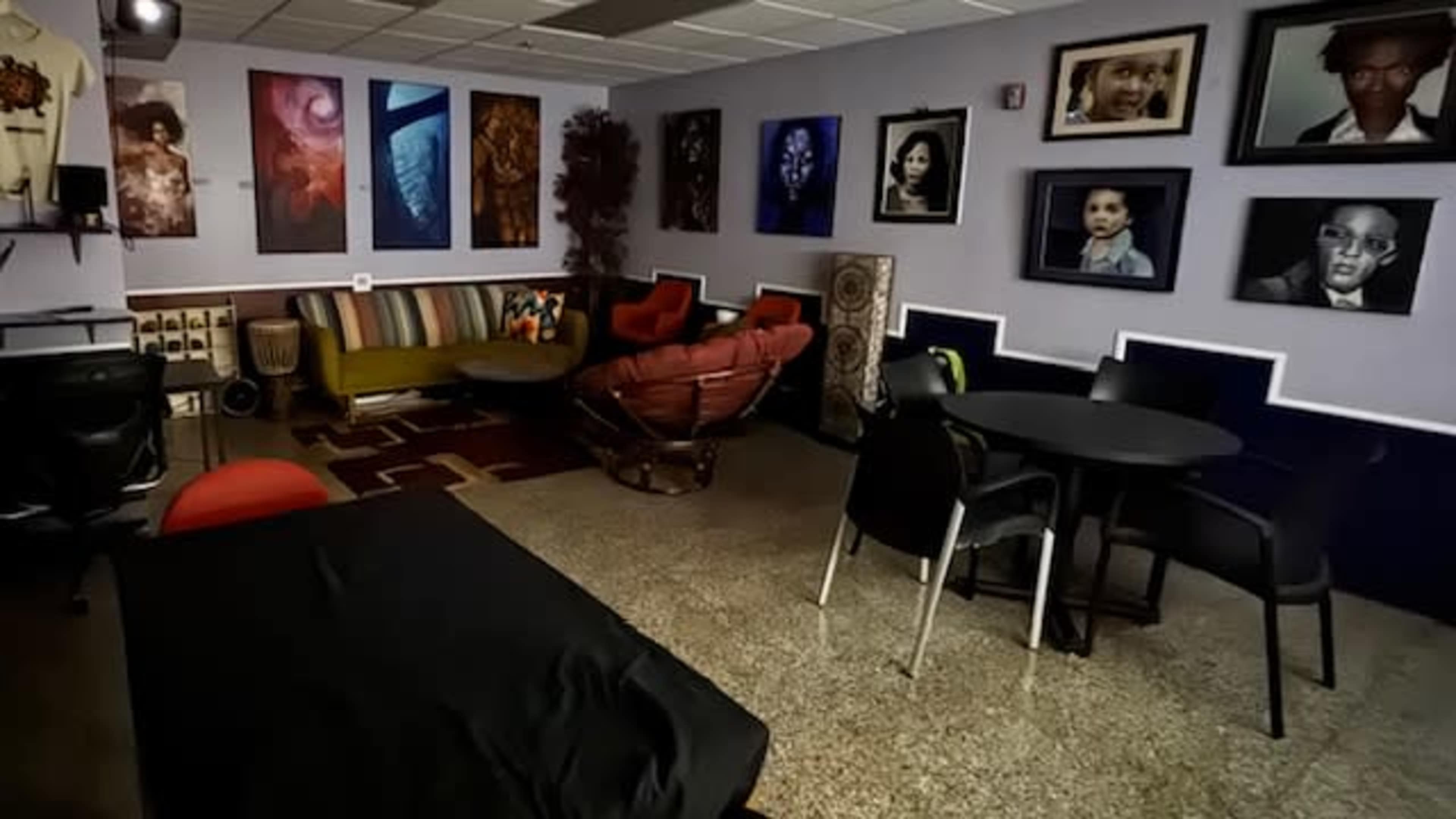 The image shows a well-lit room featuring a variety of seating arrangements, decorative artwork on the walls, and a mix of modern and comfortable furniture.