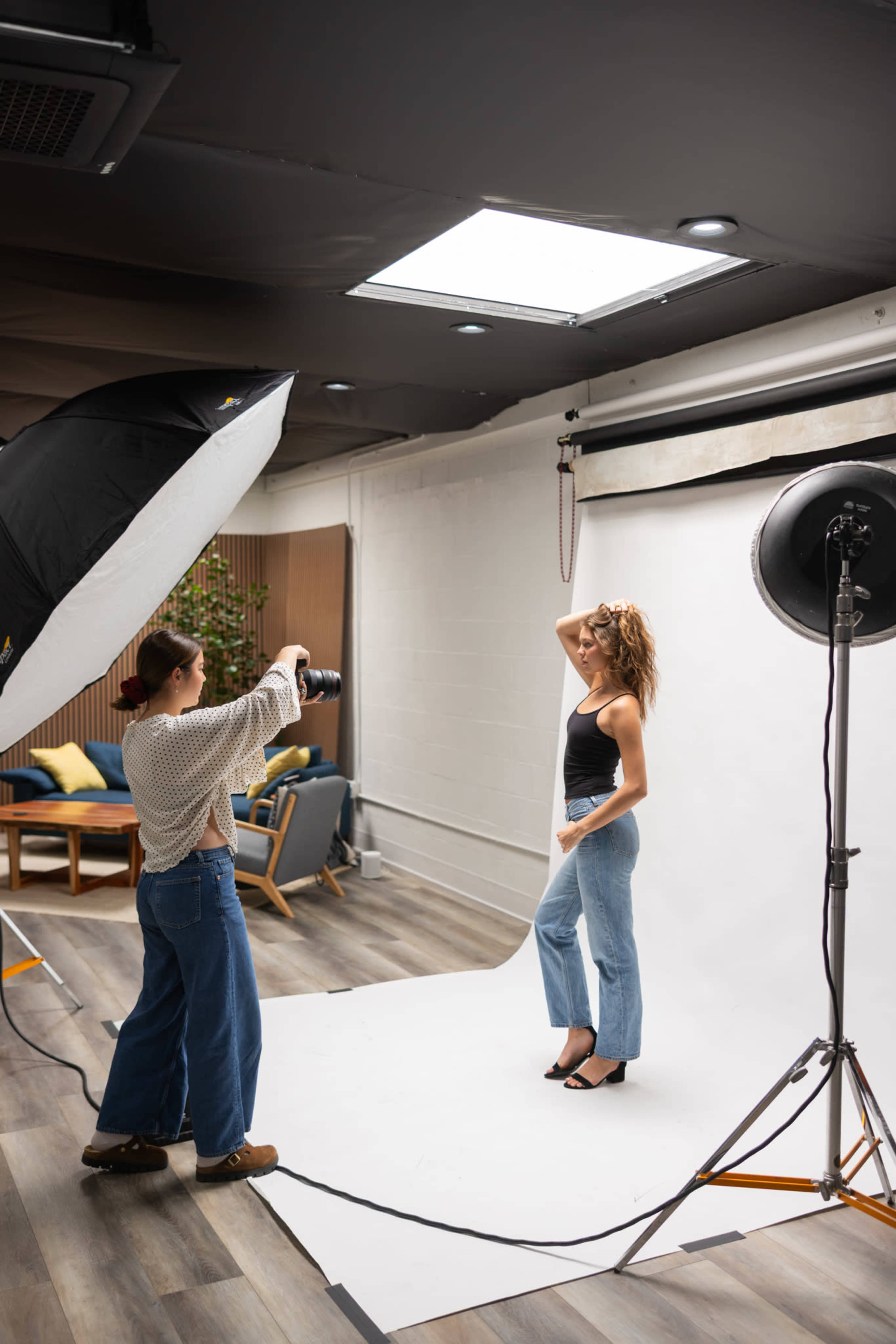 A photographer captures a model posing in a studio setting with a backdrop and soft lighting equipment.