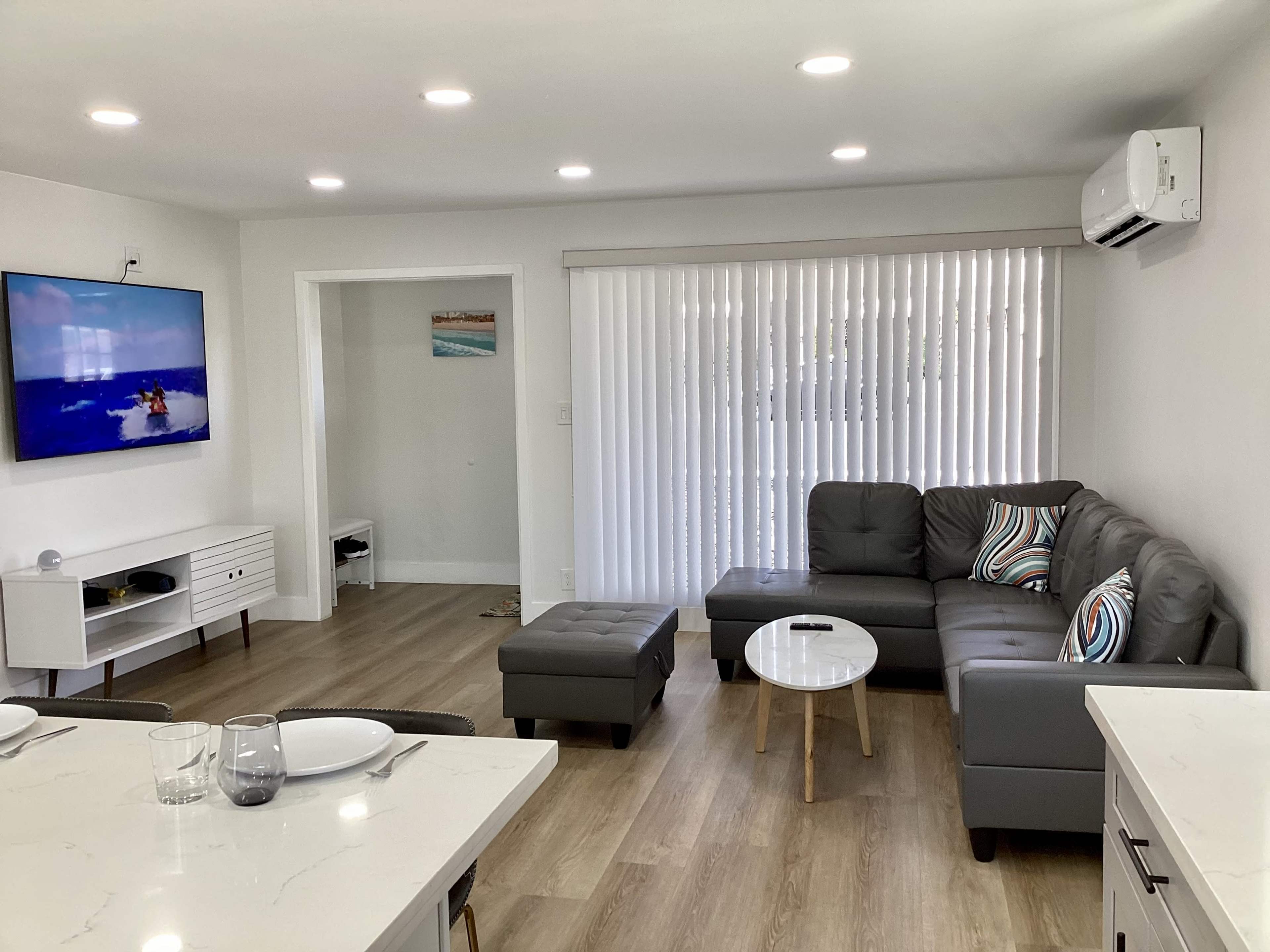 A modern living room with a gray sectional sofa, a coffee table, and a mounted television displaying a vibrant scene.