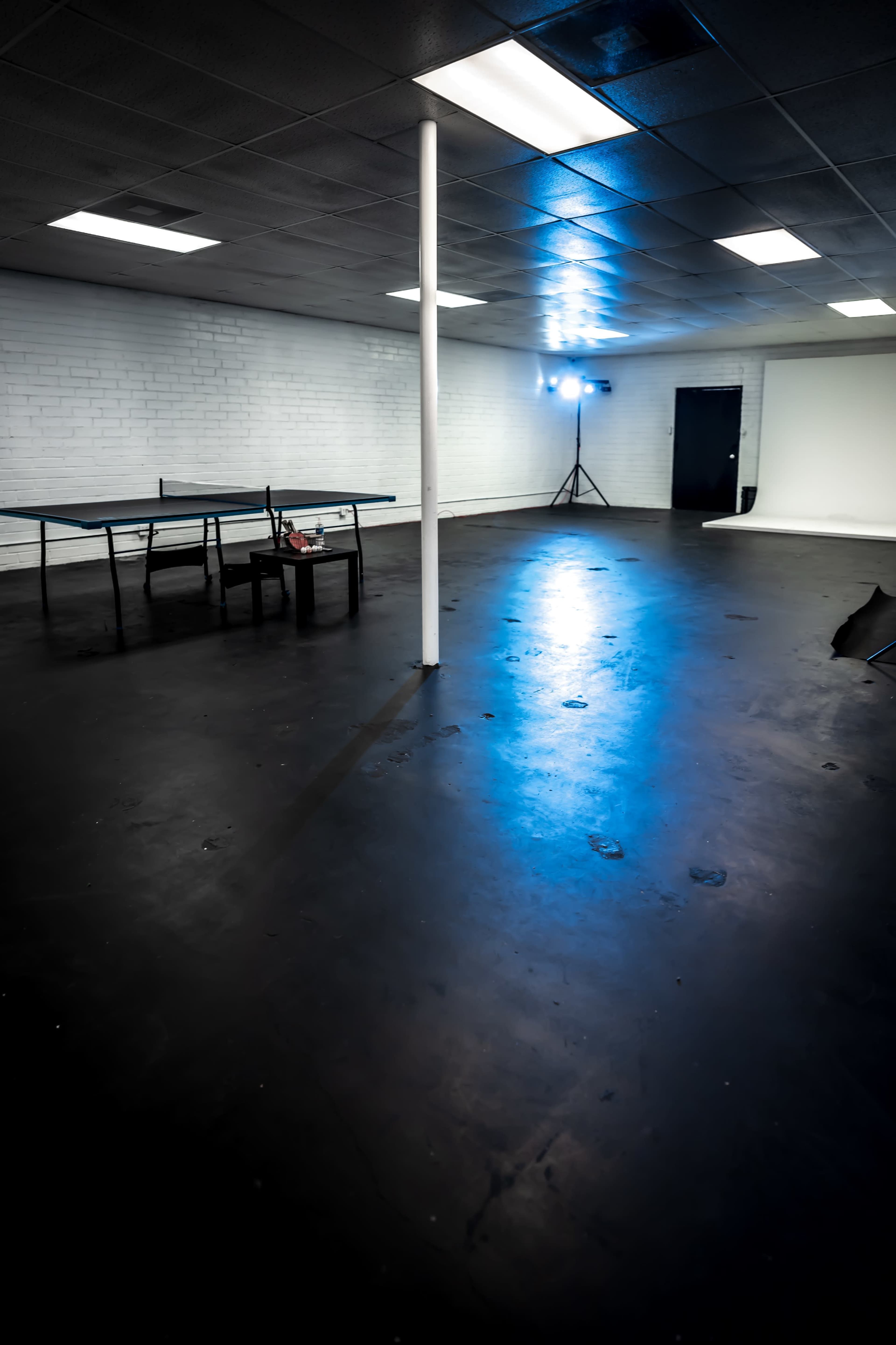 An empty room with a black floor, a table in the center, and a spotlight illuminating one corner.