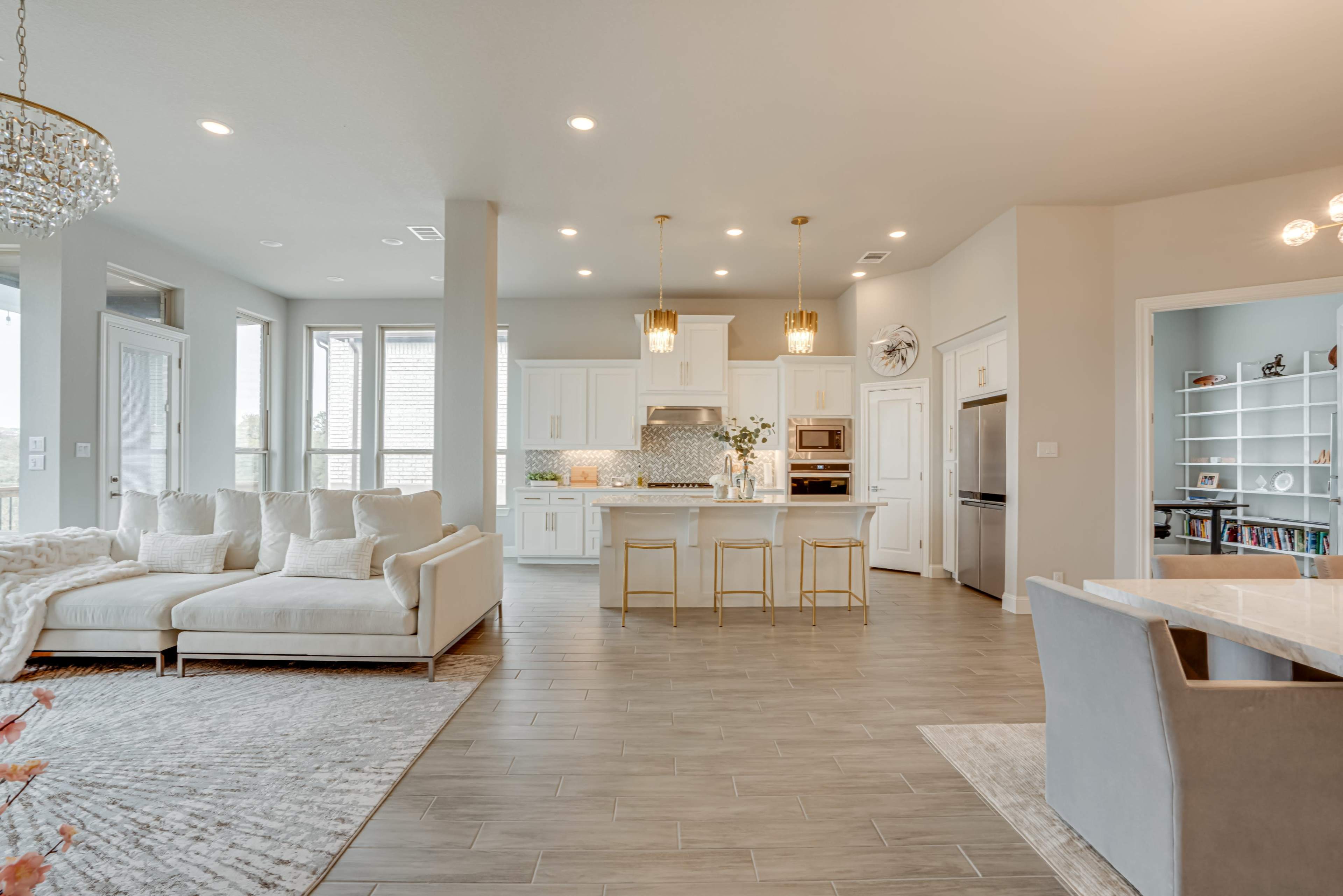 A modern living room and kitchen area with a white sectional sofa, a dining table, and an island with bar stools.