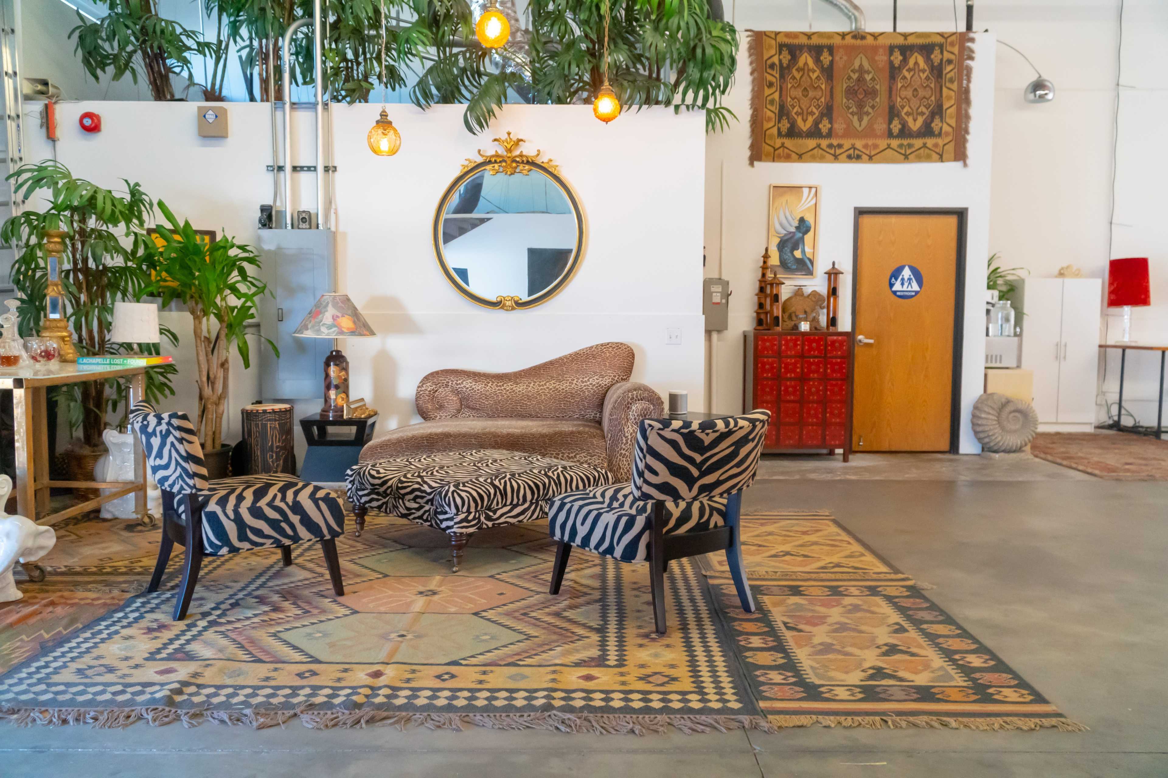 A stylish sitting area with a zebra-patterned sofa and two matching chairs on a decorative rug surrounded by various plants and wall decor.