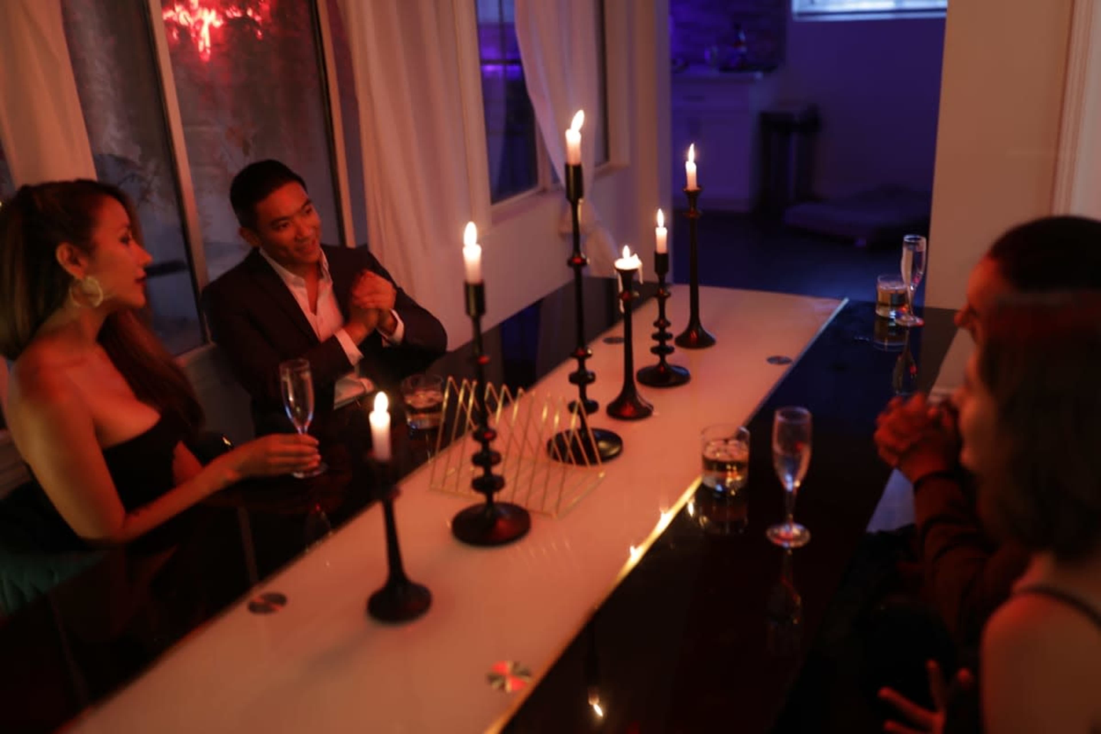 A group of four people sits around a dimly lit table with candles and drinks, engaged in conversation.