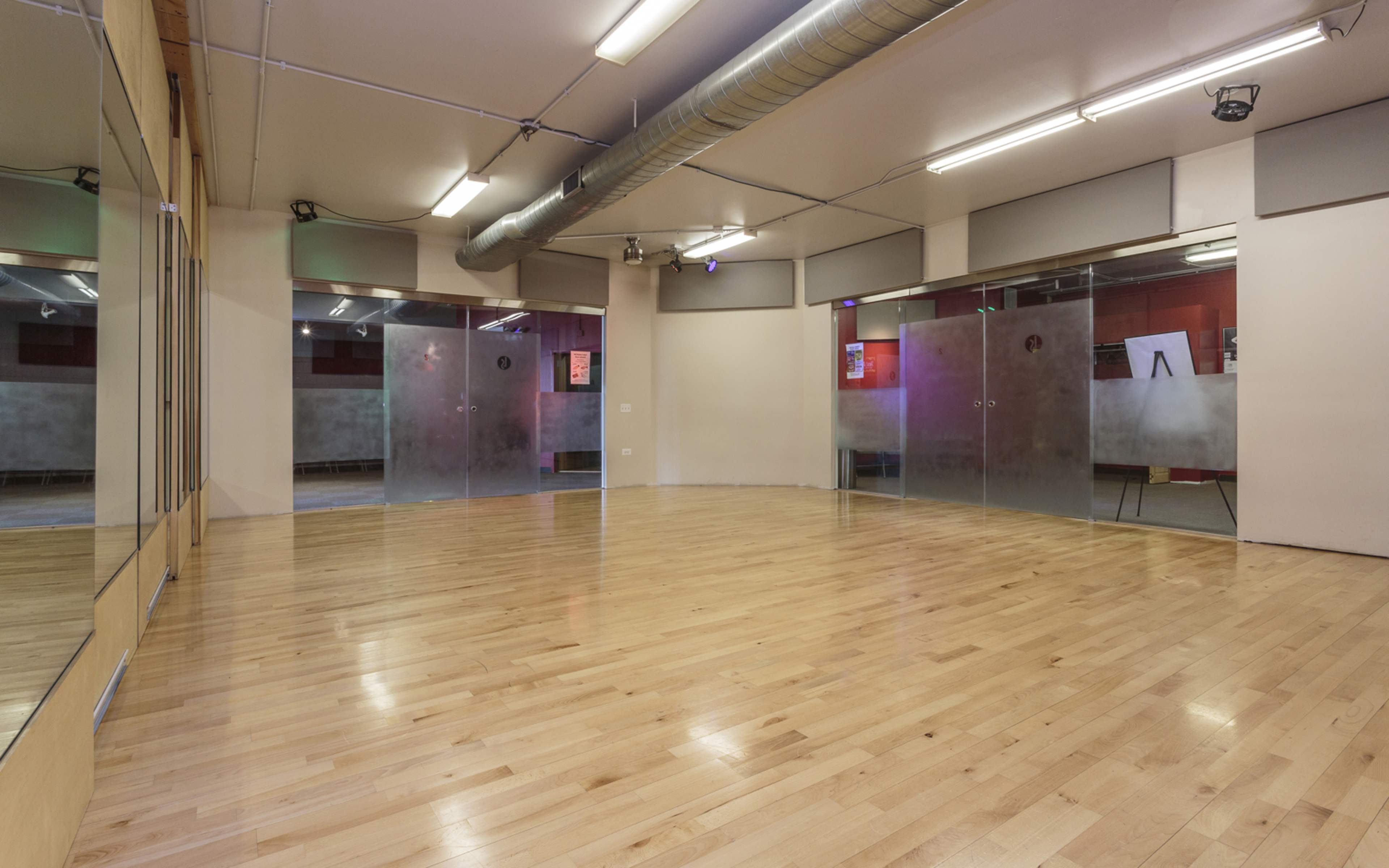 An empty studio space with wooden flooring and large glass doors.