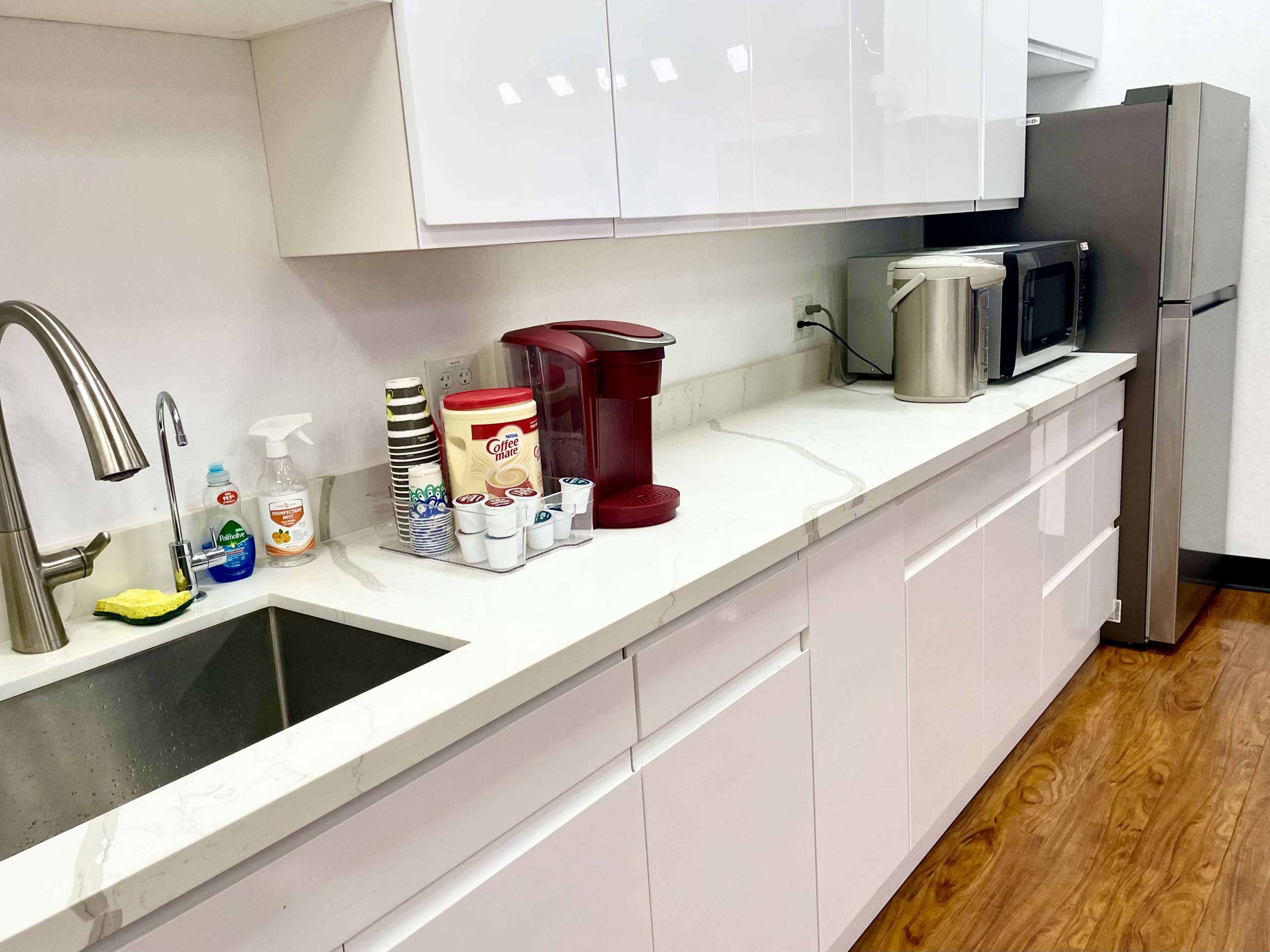 A modern kitchen with a sink, coffee maker, microwave, and a refrigerator along a clean countertop.