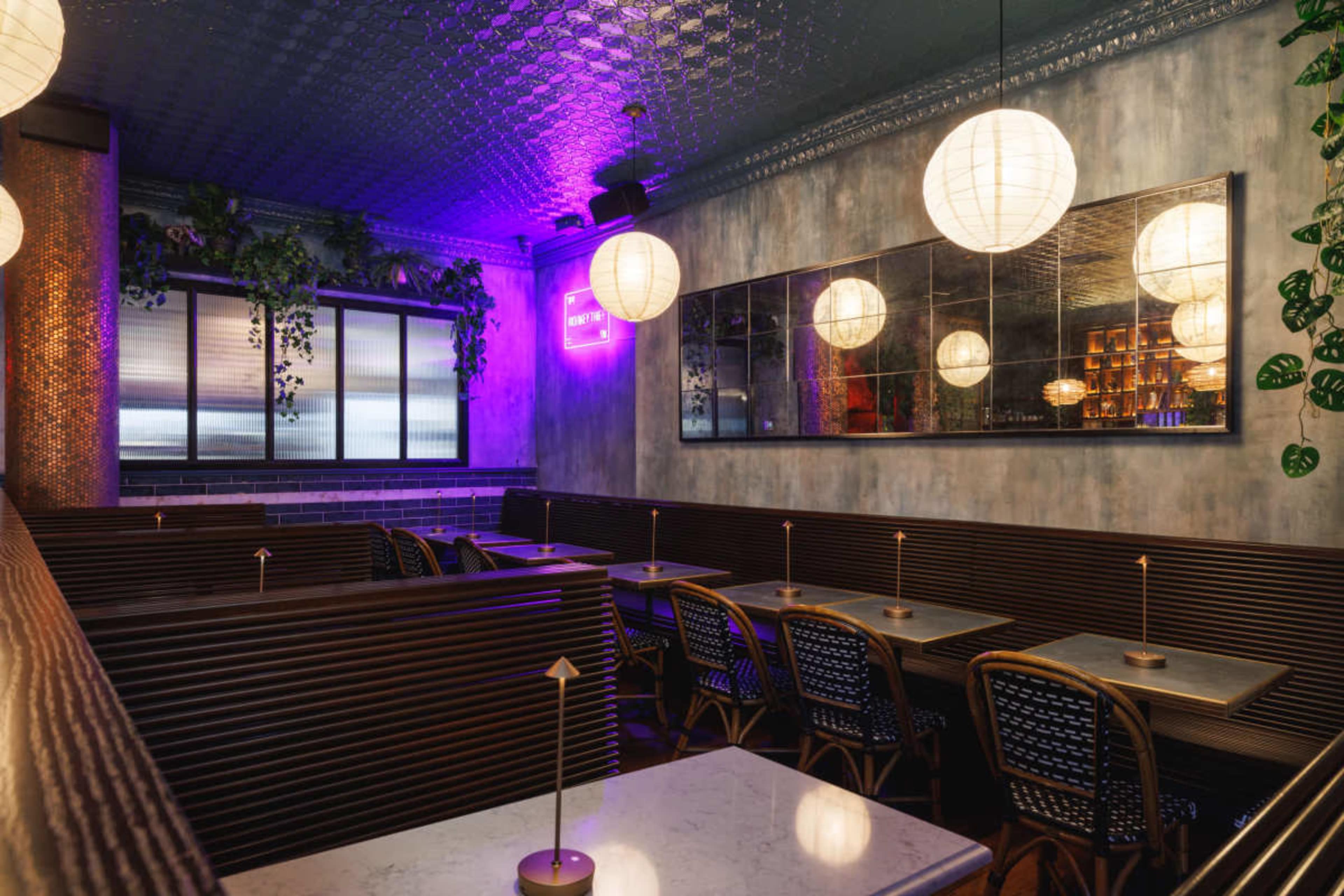 The image depicts an elegantly designed restaurant interior with wooden seating, tables, and illuminated paper lanterns hanging from the ceiling.