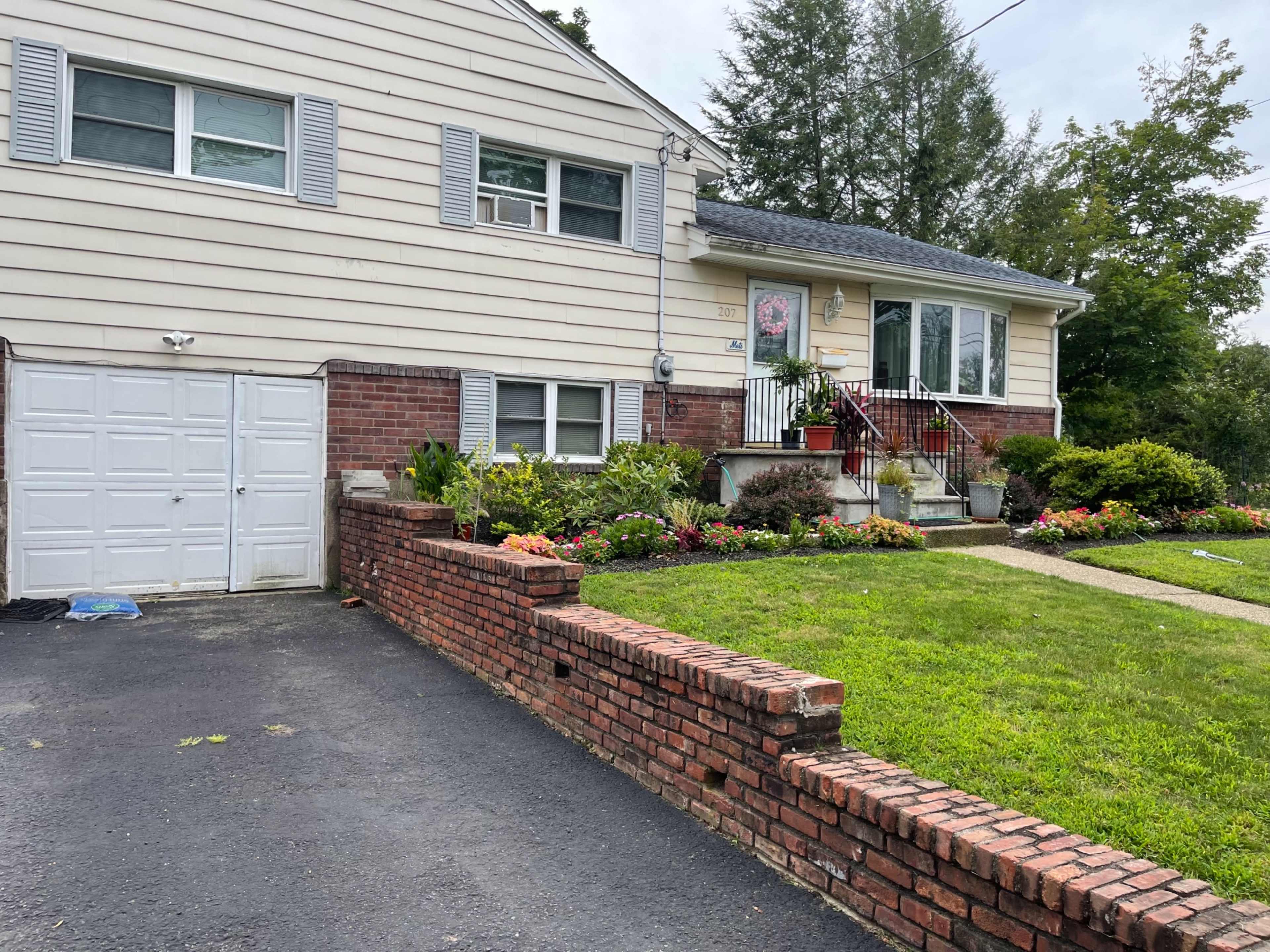 A two-story house with a brick front wall, a garage, and a well-maintained flower garden in the front yard.