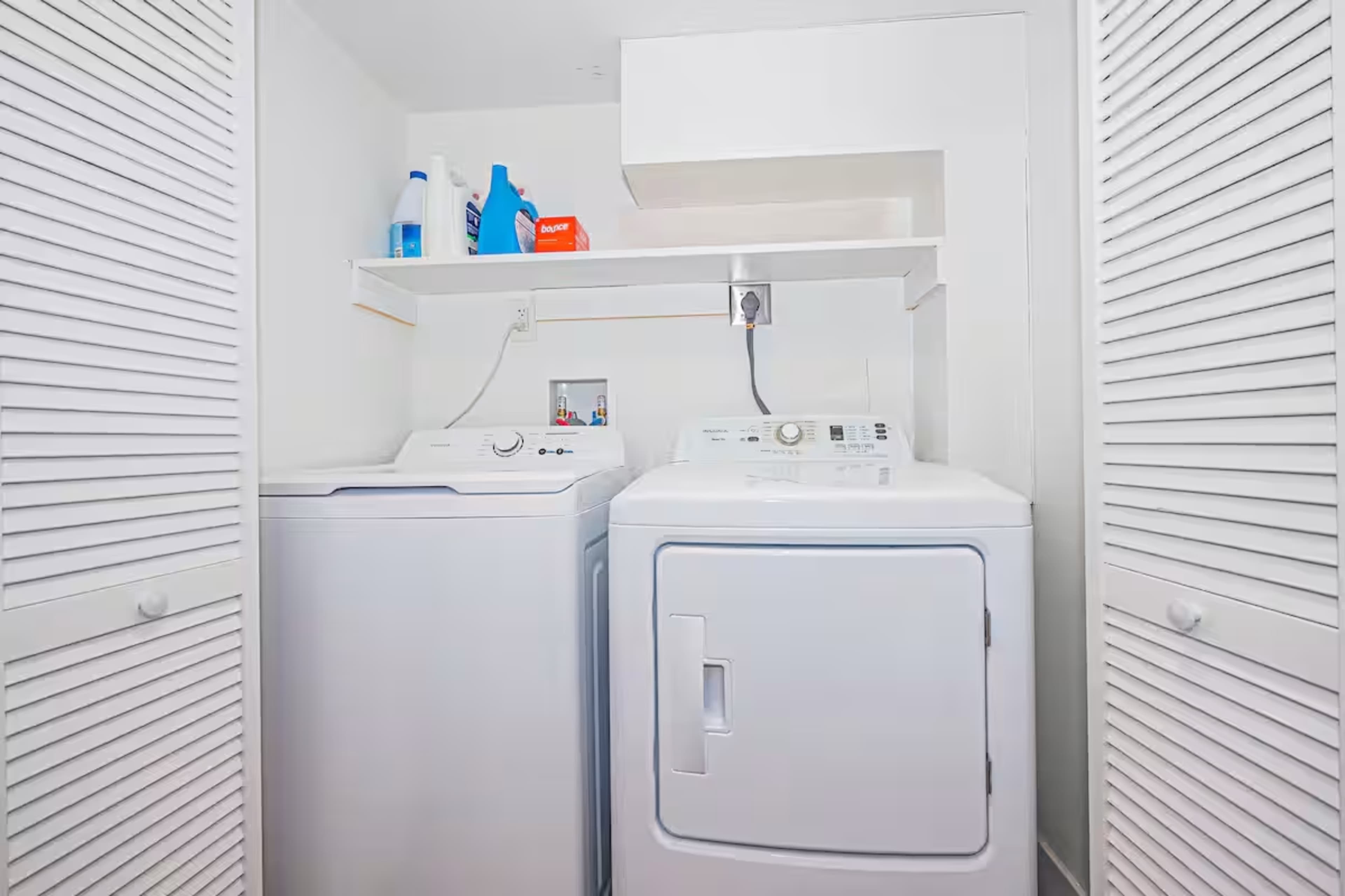 The image shows a laundry area featuring a washer and dryer side by side with shelves above them for laundry supplies.