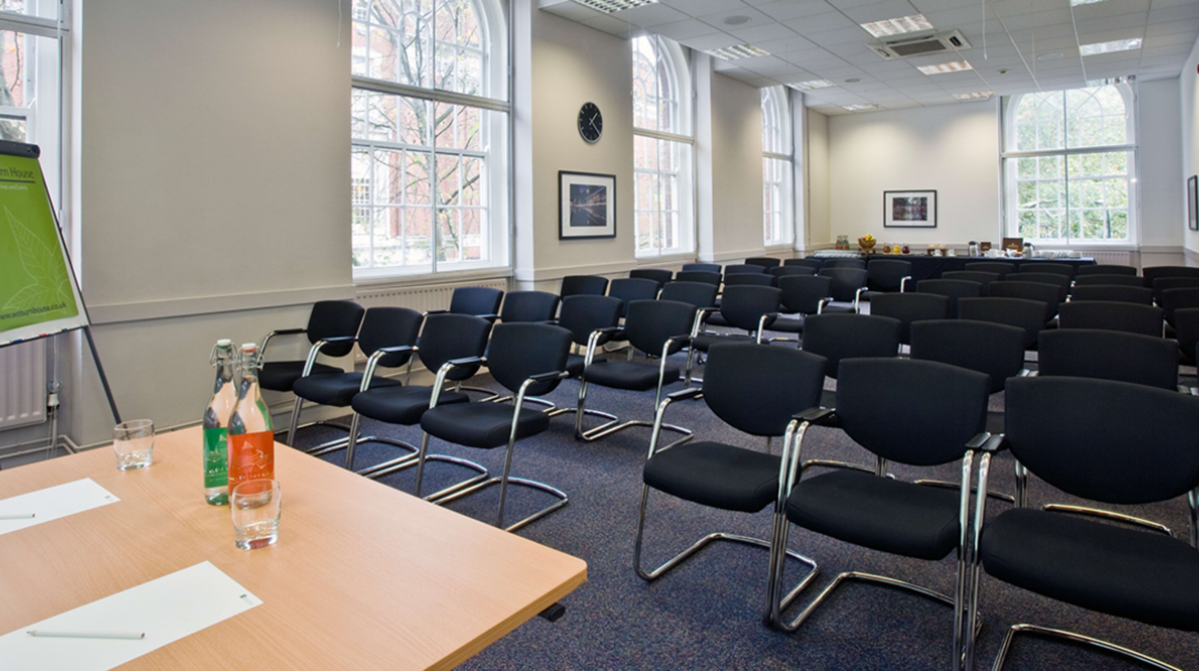 The image shows a meeting room with several rows of empty black chairs facing a small table with two bottles of water and glasses.