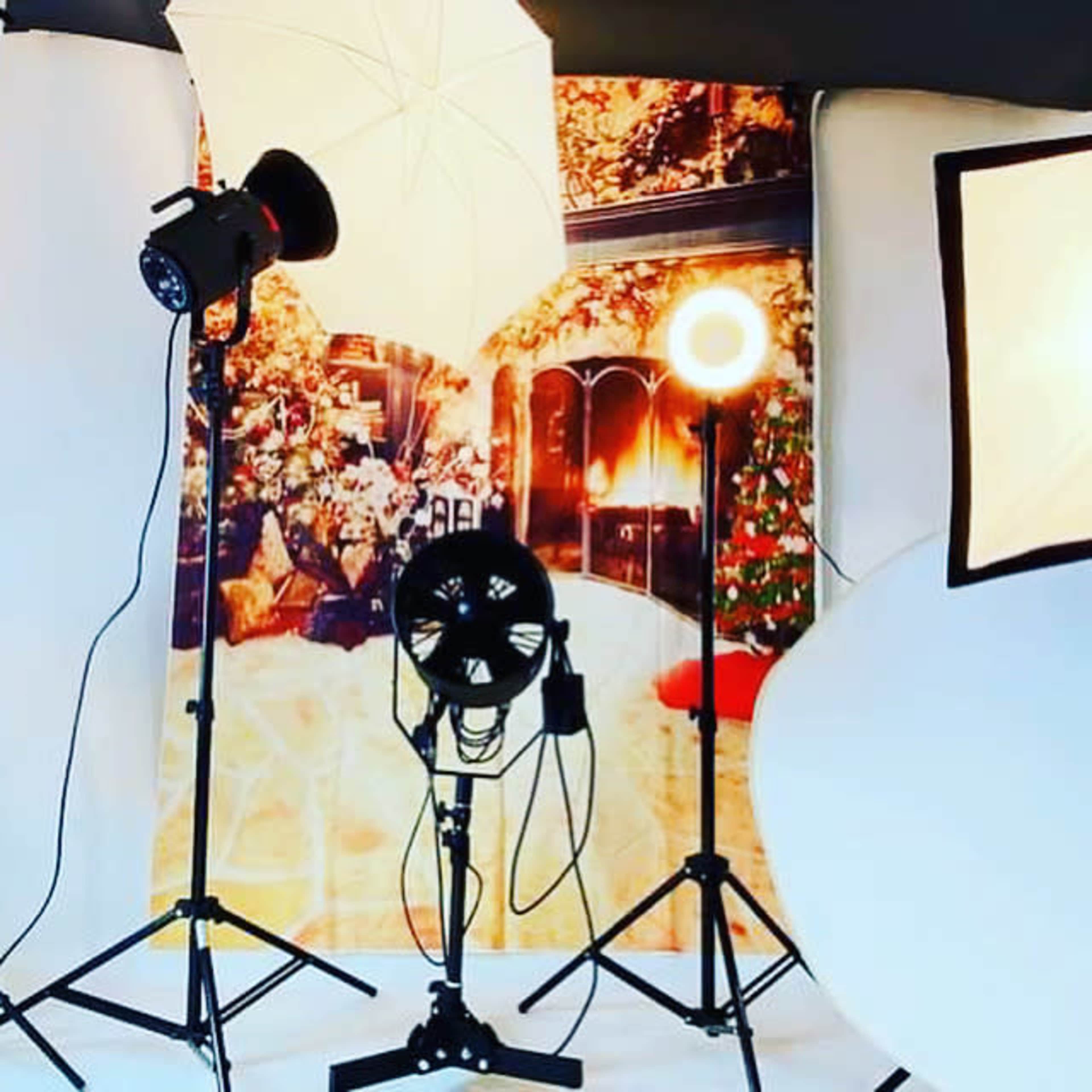 Studio lighting equipment arranged in front of a backdrop depicting a cozy indoor scene with a fireplace and Christmas decorations.