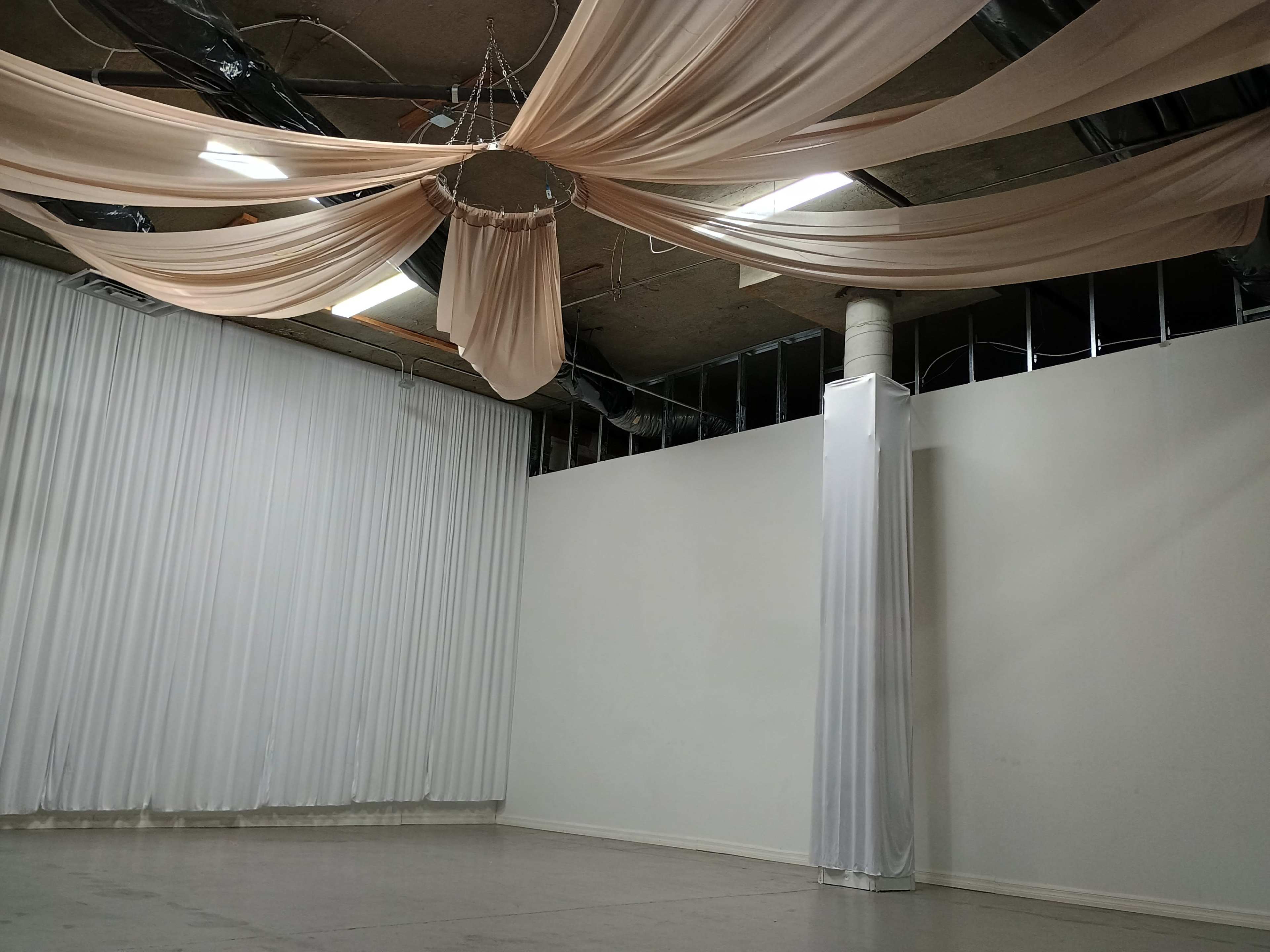 The image depicts a spacious indoor area with draped fabric on the ceiling and walls, creating a minimalistic aesthetic.