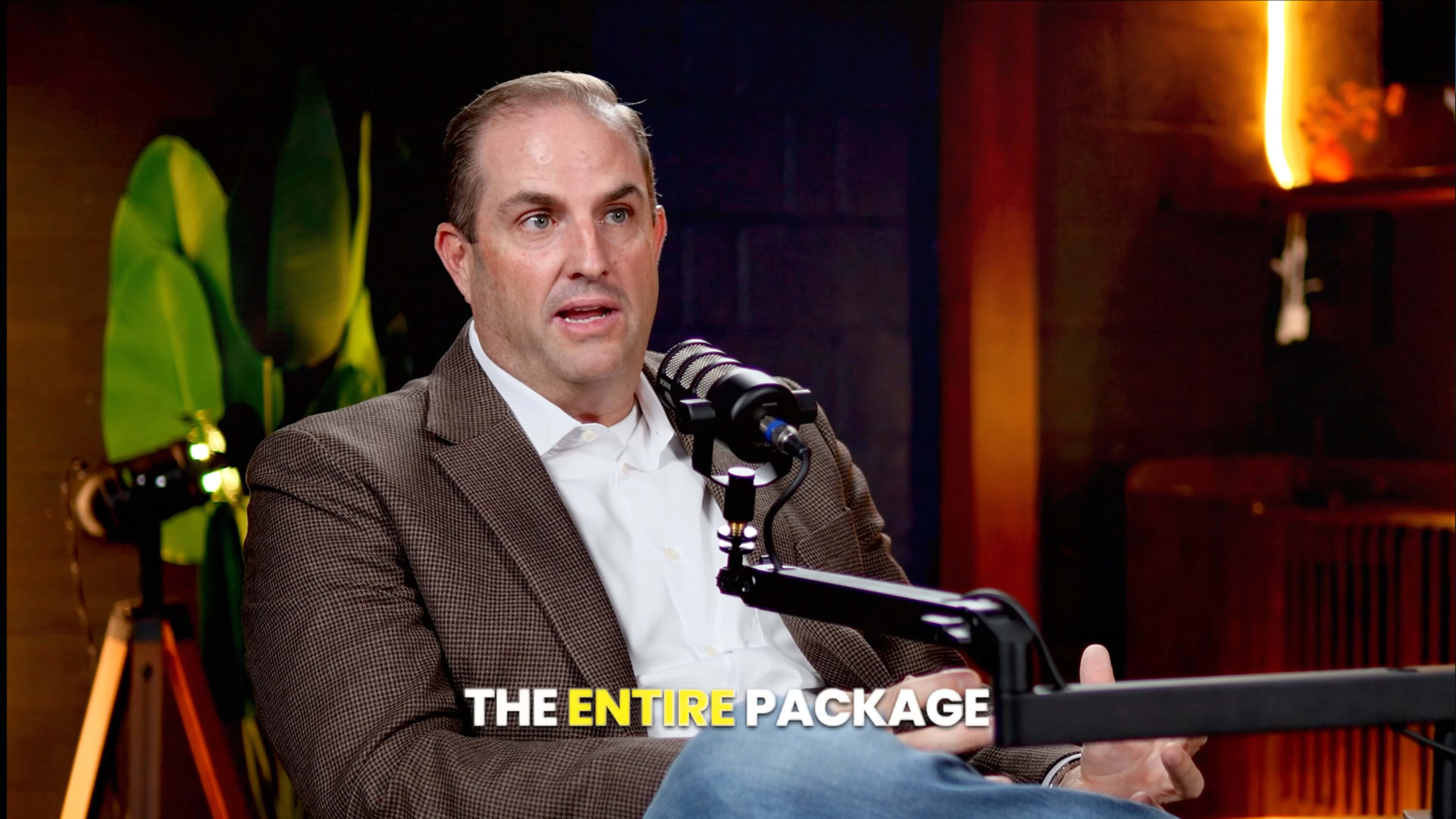A man in a brown checkered blazer speaks into a microphone during a recording session.