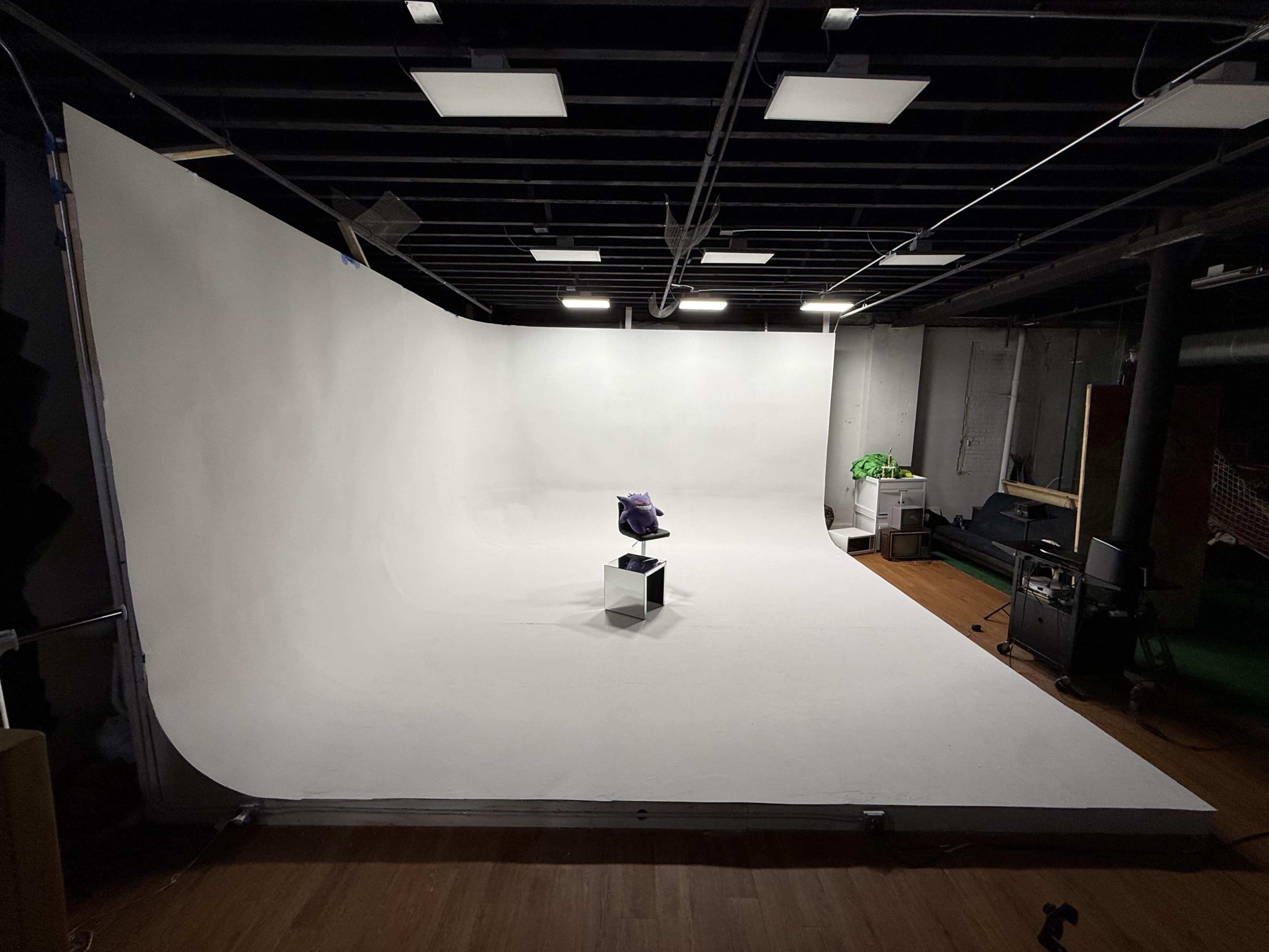 The image shows a spacious photo studio with a seamless white backdrop, featuring a single purple object placed on a clear cube in the center.