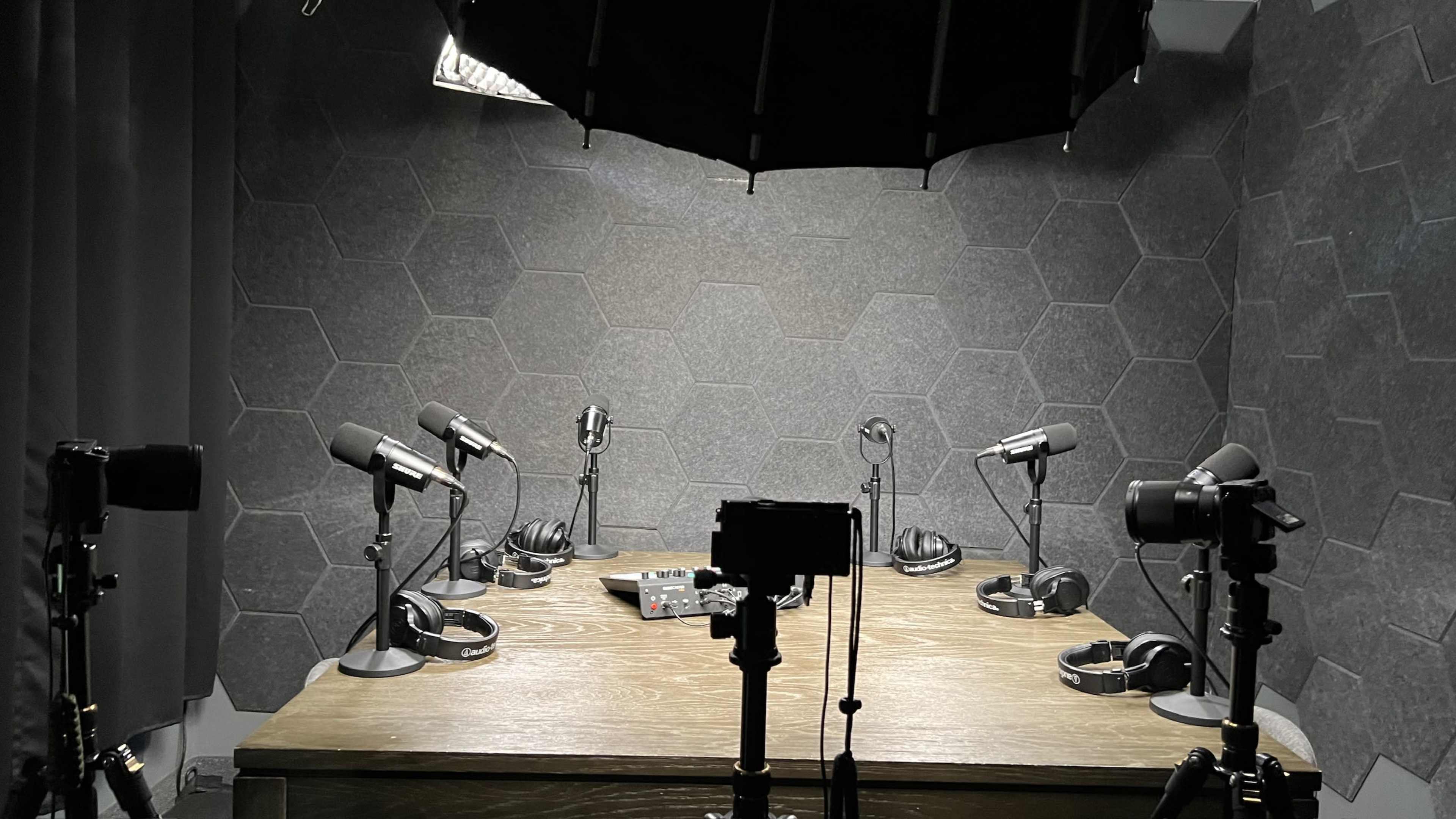 A multi-camera setup for a podcast recording is arranged on a wooden table, featuring microphones and headphones positioned around it.