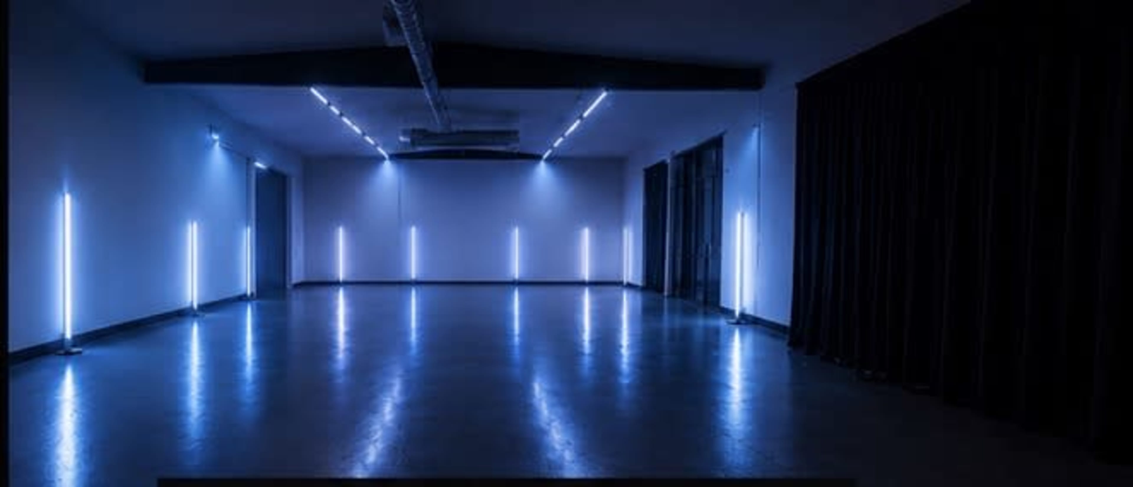 A spacious, dimly lit room features several vertical blue light fixtures.