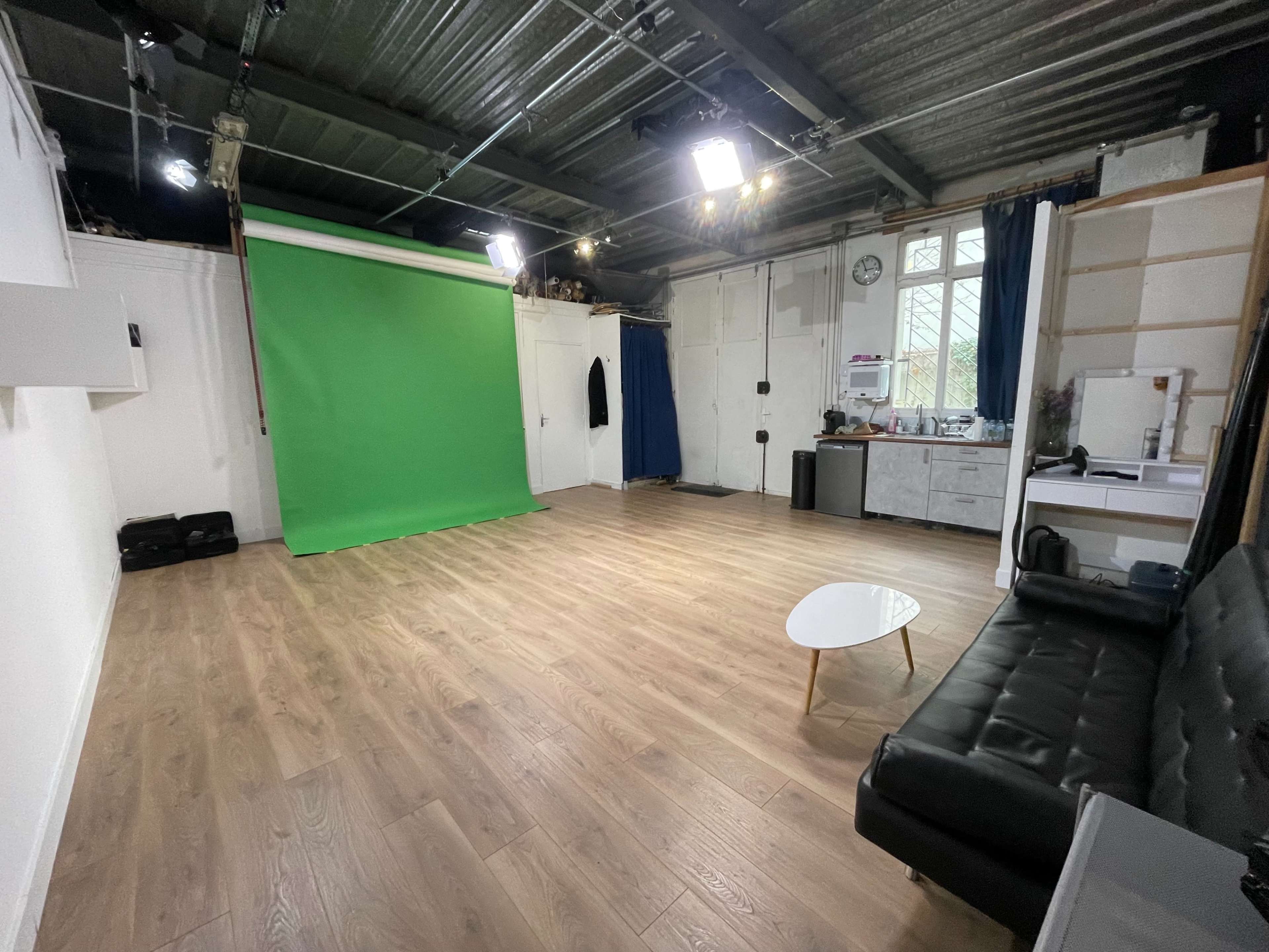 A spacious room with a green backdrop, wooden flooring, and minimal furniture including a black couch and a small table.
