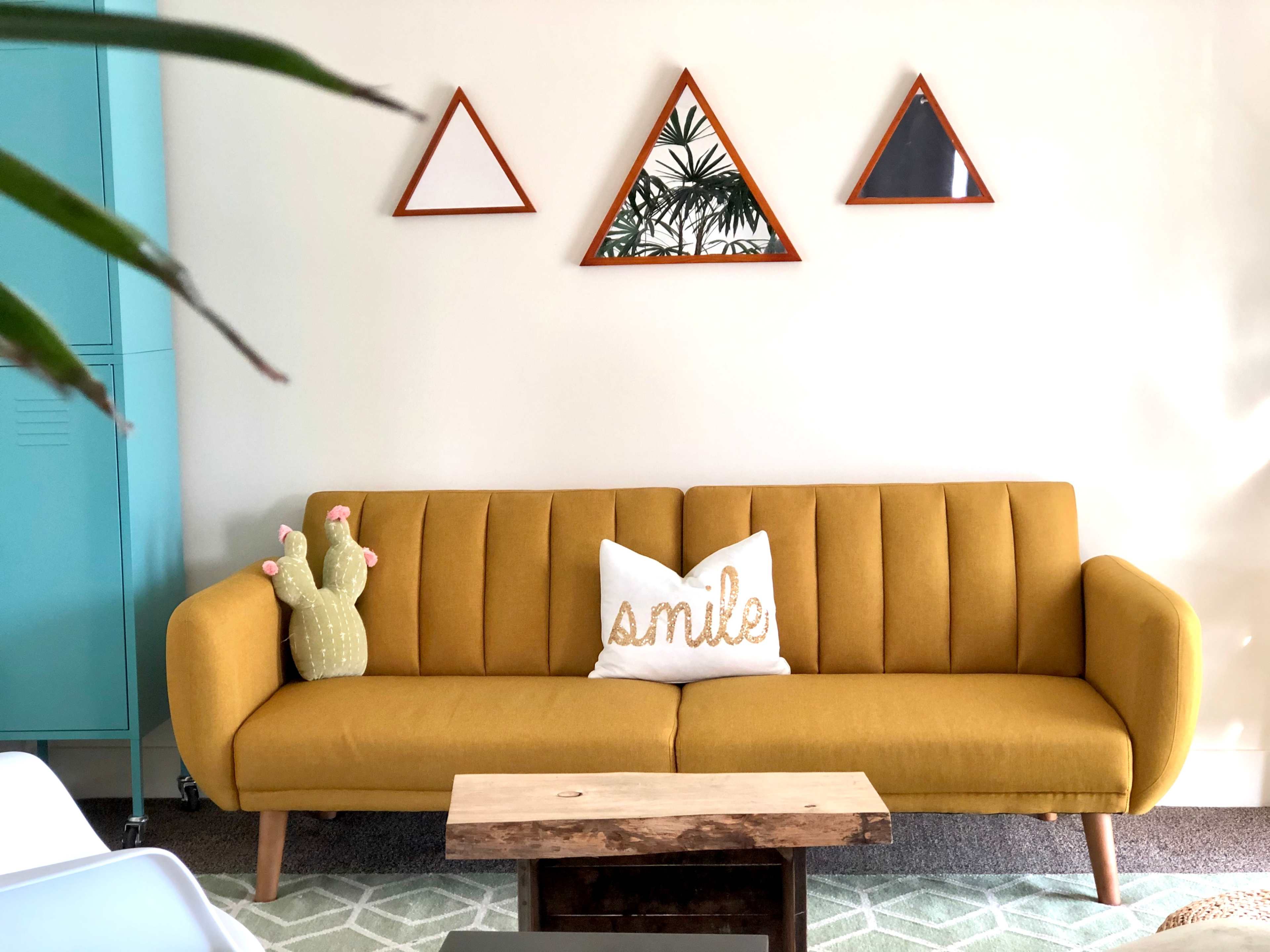 A mustard yellow sofa is positioned against a light wall, adorned with triangular decorations and a wooden coffee table in front.