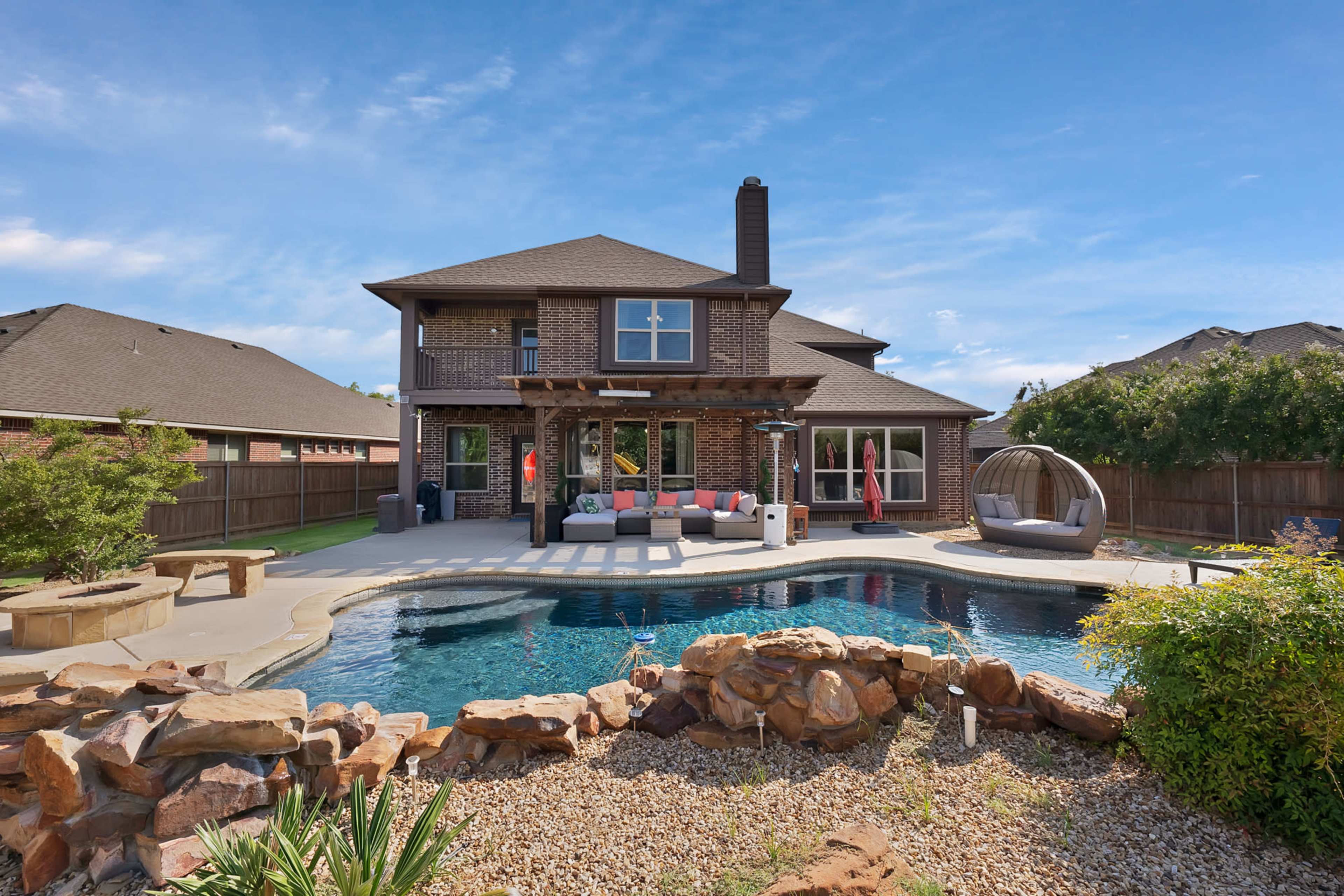 A two-story house with a backyard pool and patio area is surrounded by well-maintained landscaping and a wooden fence.