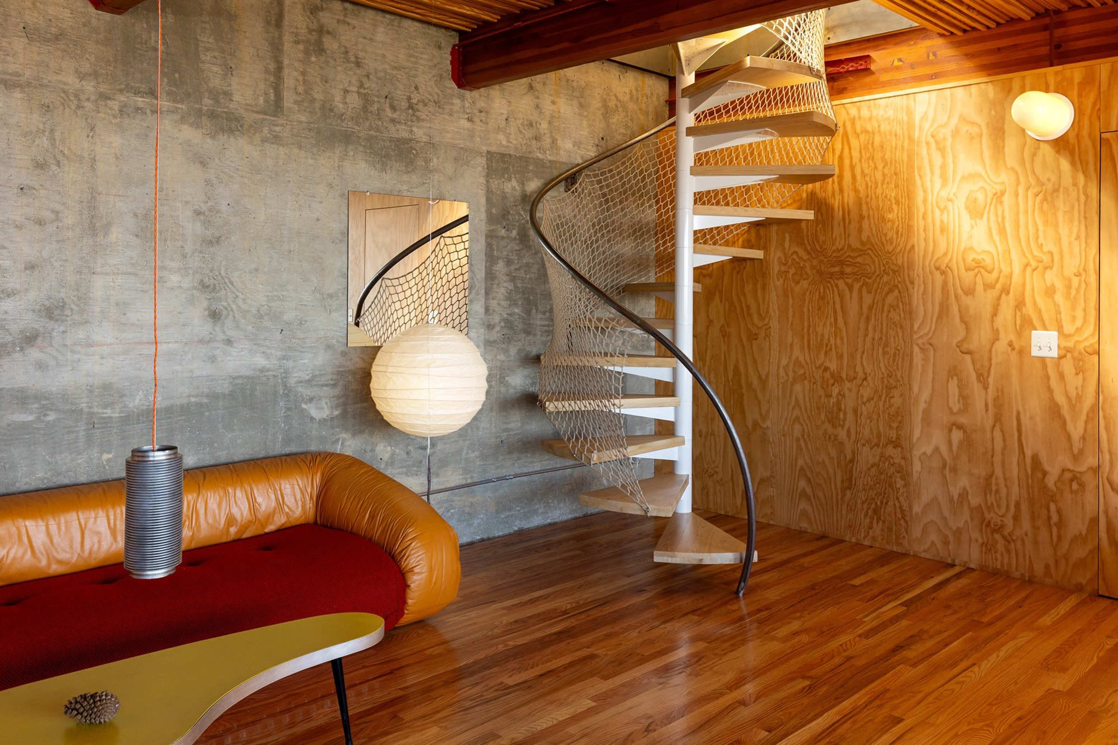 The image features a modern interior with a spiral staircase, a sectional sofa, and wooden paneling.