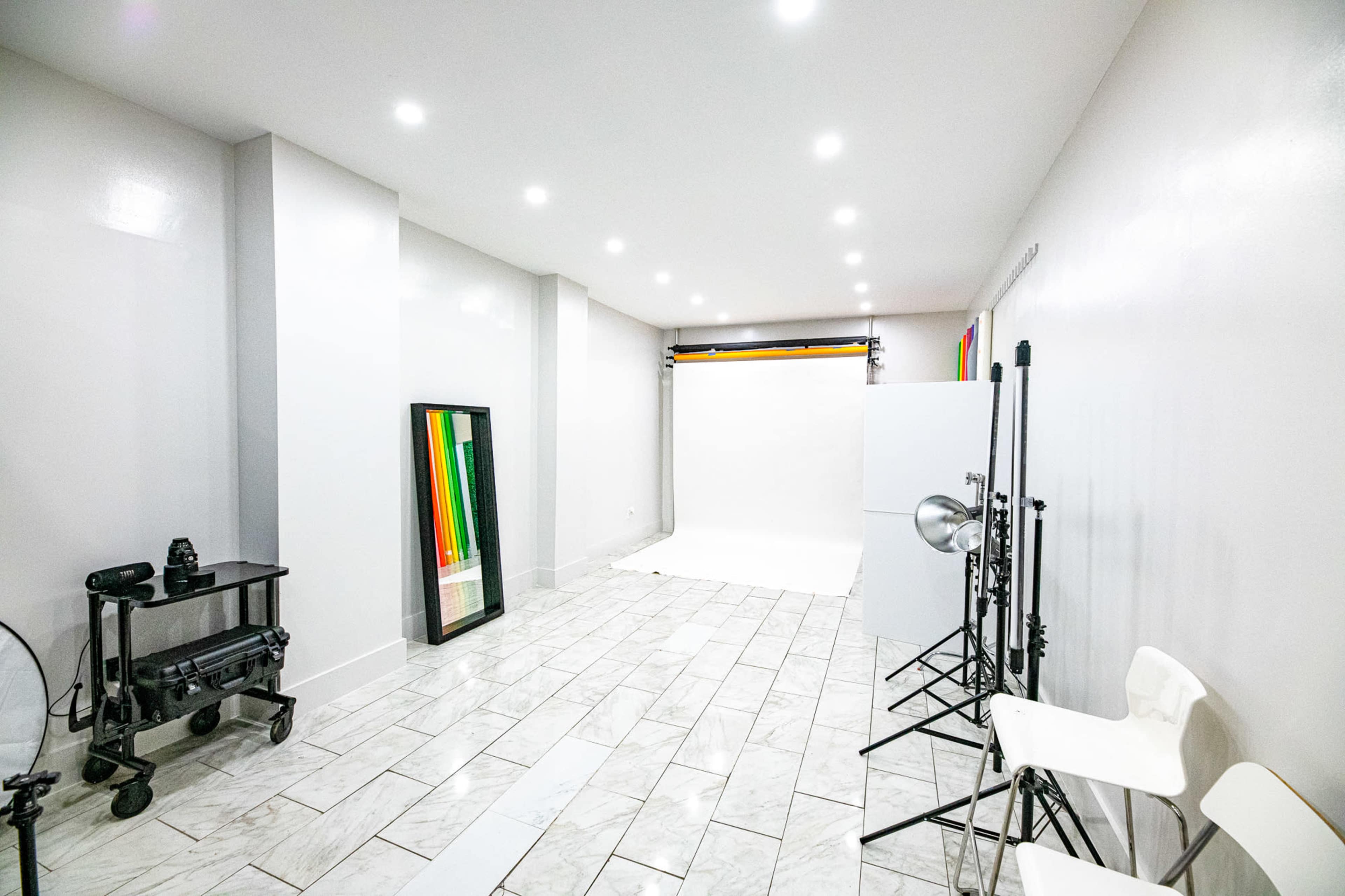 A spacious photography studio with white walls, a seamless backdrop, and various equipment including tripods and lights.
