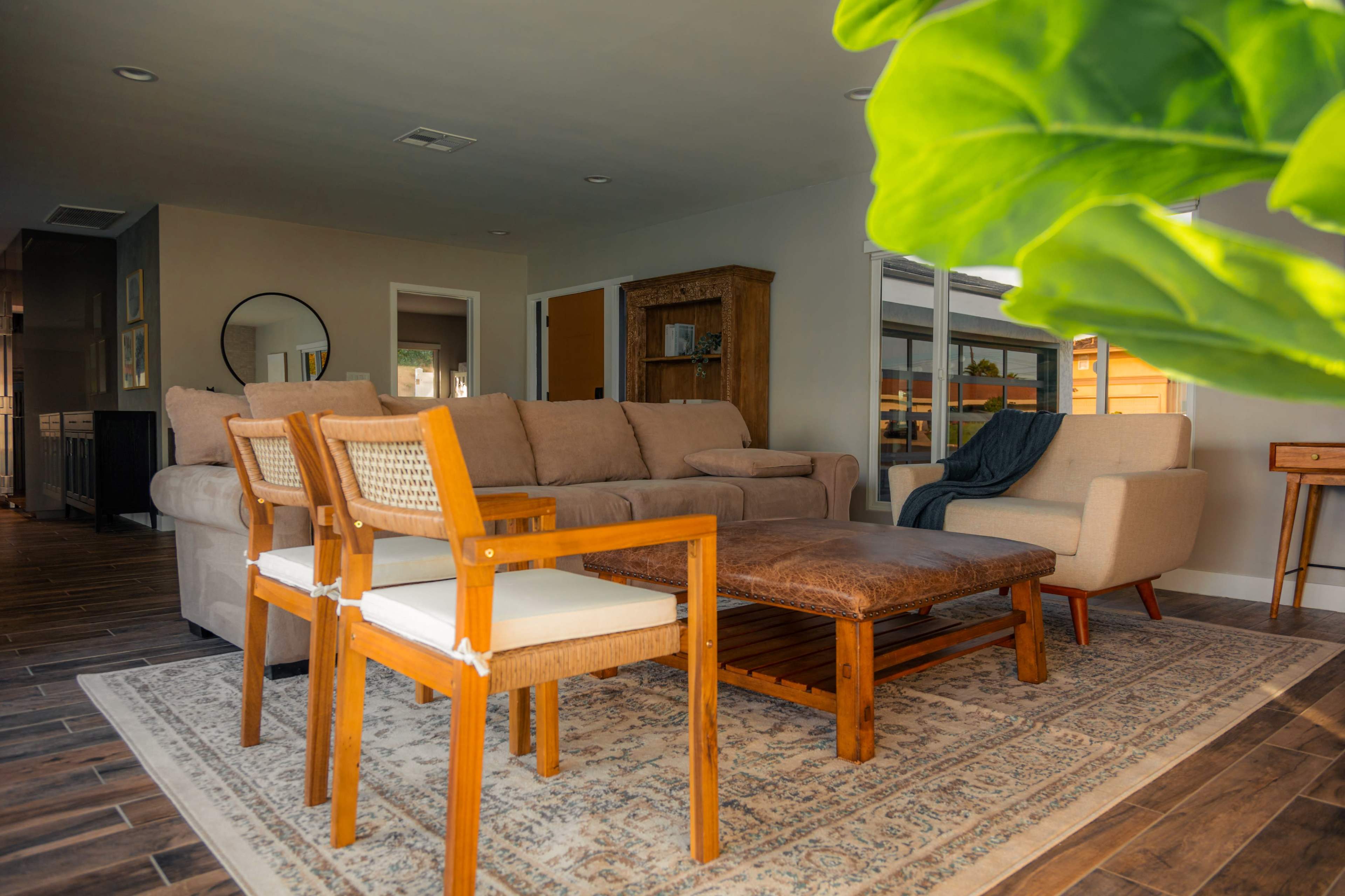 A modern living room with a large beige sectional sofa, two wooden chairs, a coffee table, and a decorative area rug.