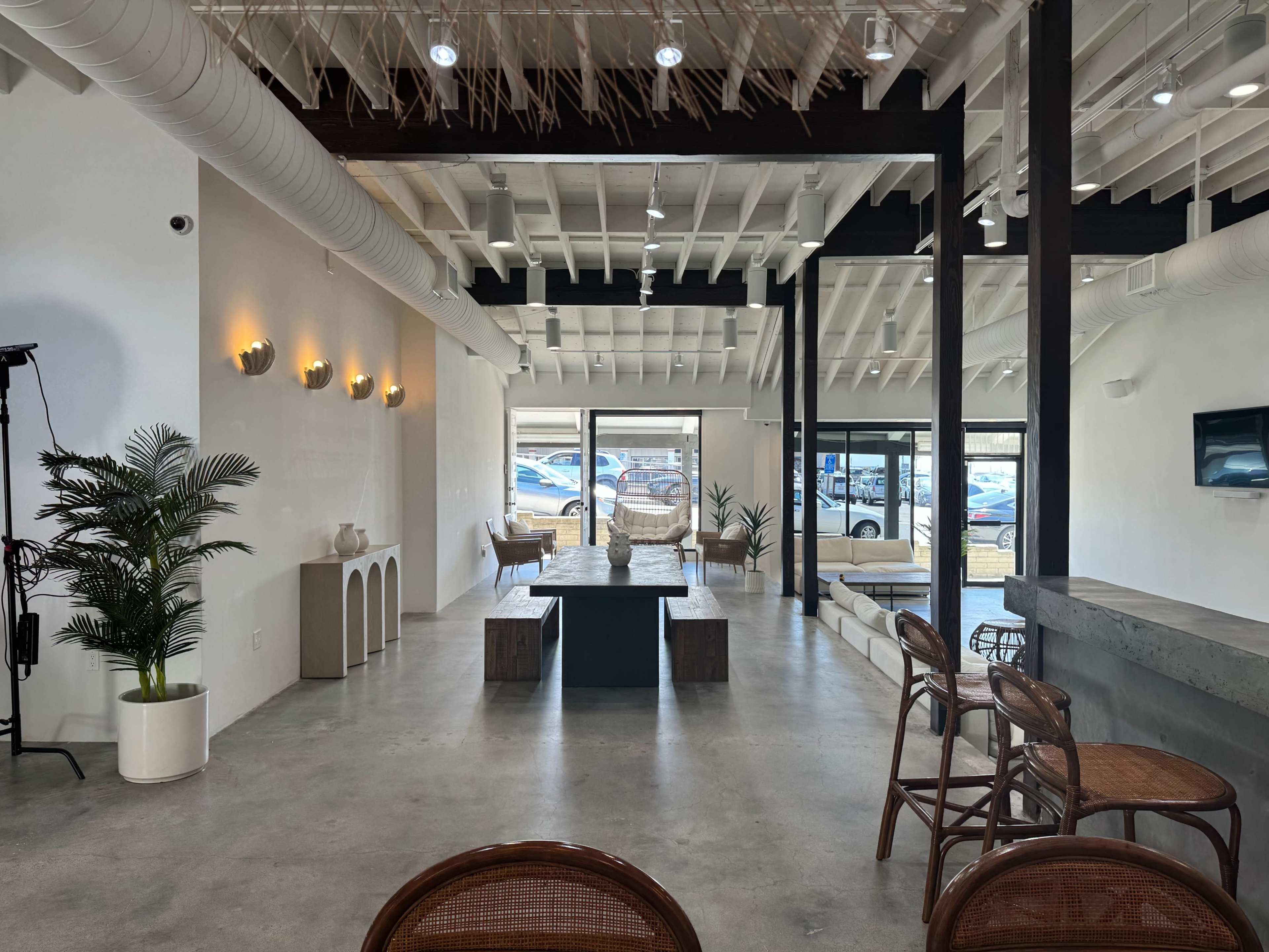 A modern, spacious interior of a venue with a central seating area, concrete flooring, and large windows that provide a view of parked cars outside.