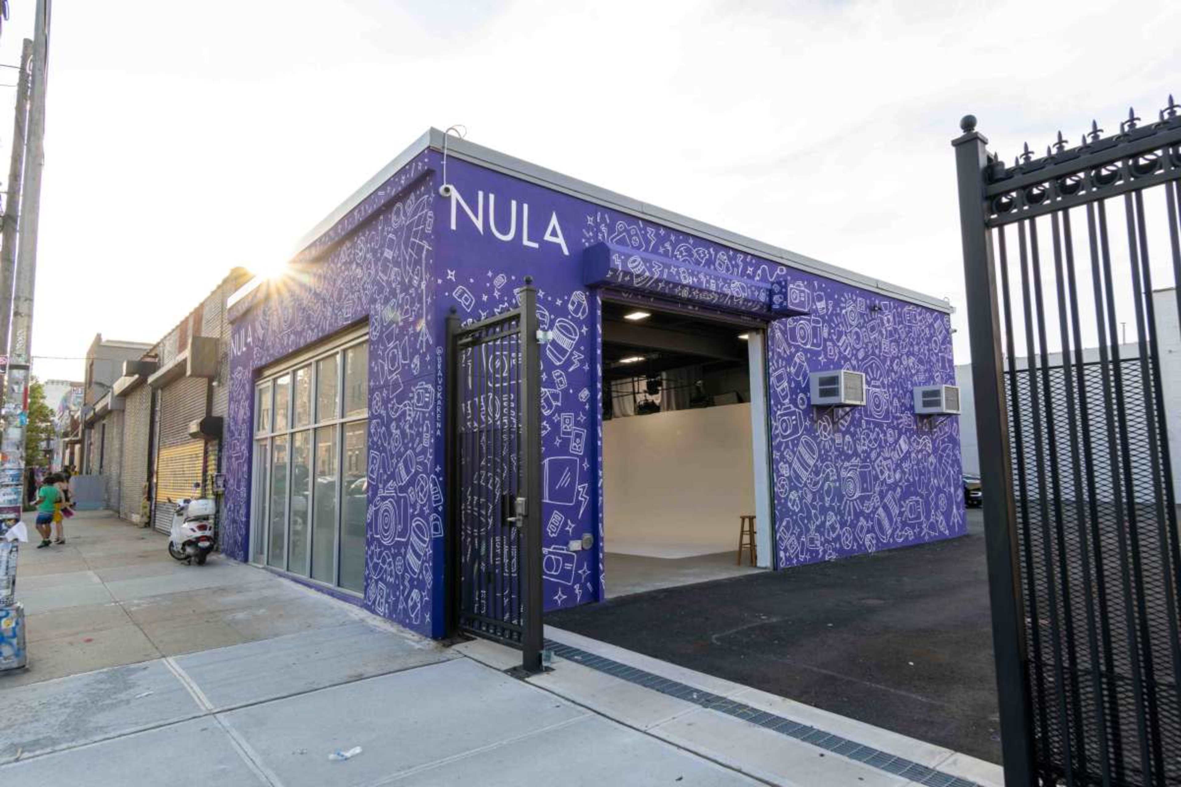The image shows a modern building with a purple exterior featuring graphic designs and large glass windows, situated on a city street.