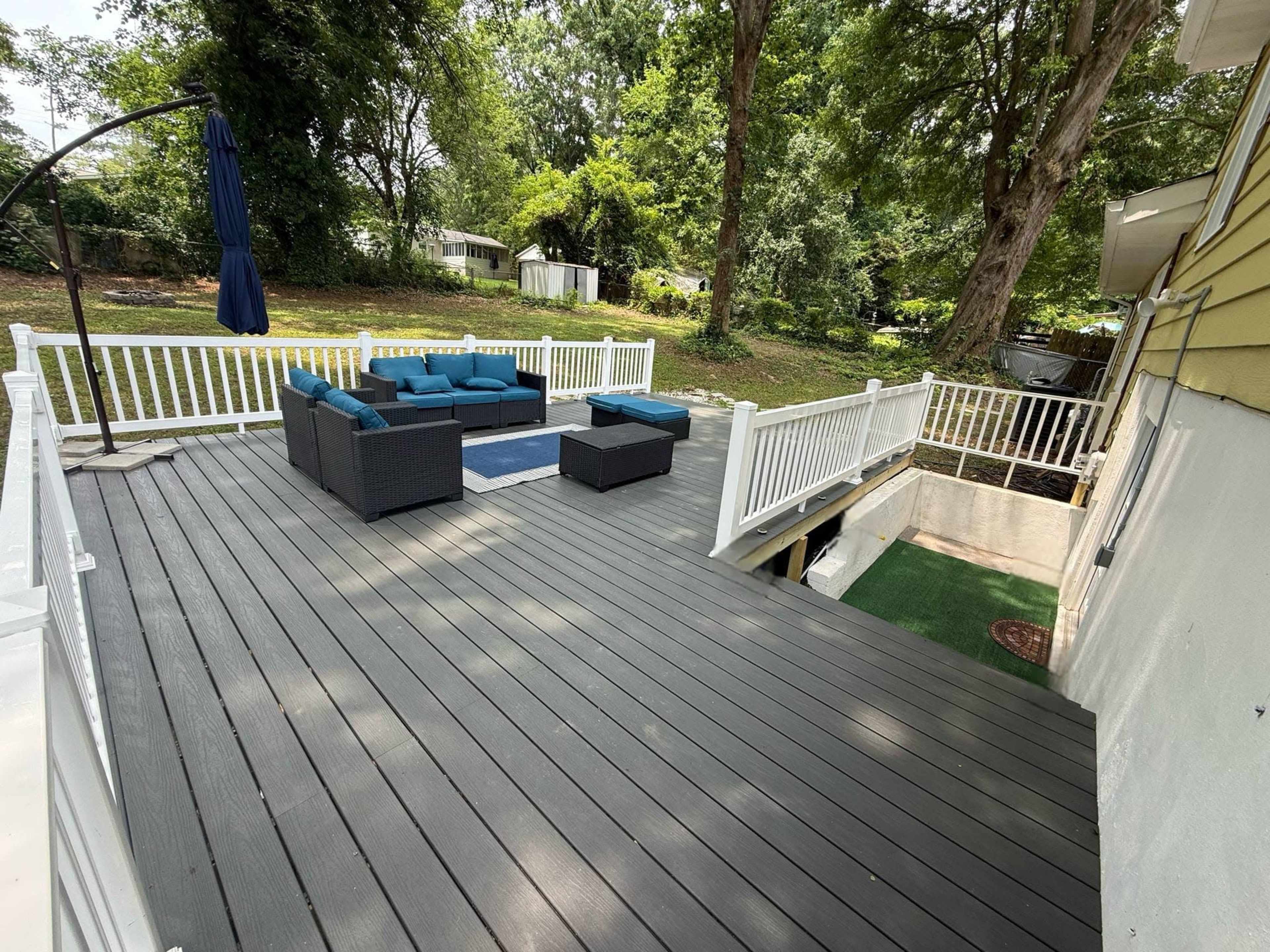 The image shows a wooden deck with outdoor seating arrangements, surrounded by greenery and residential structures in the background.