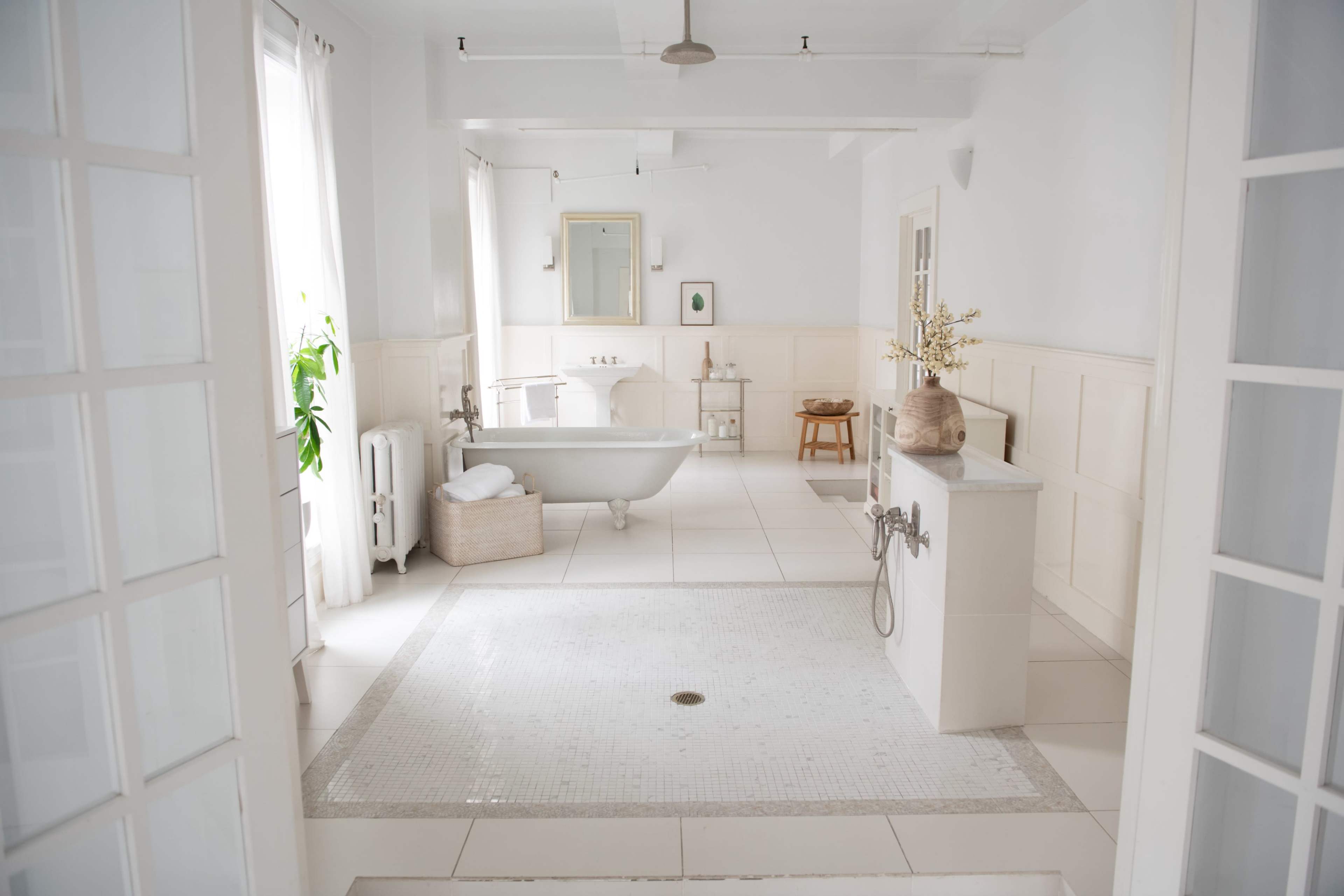 A spacious bathroom features a freestanding bathtub, a tiled floor, and large windows allowing natural light.