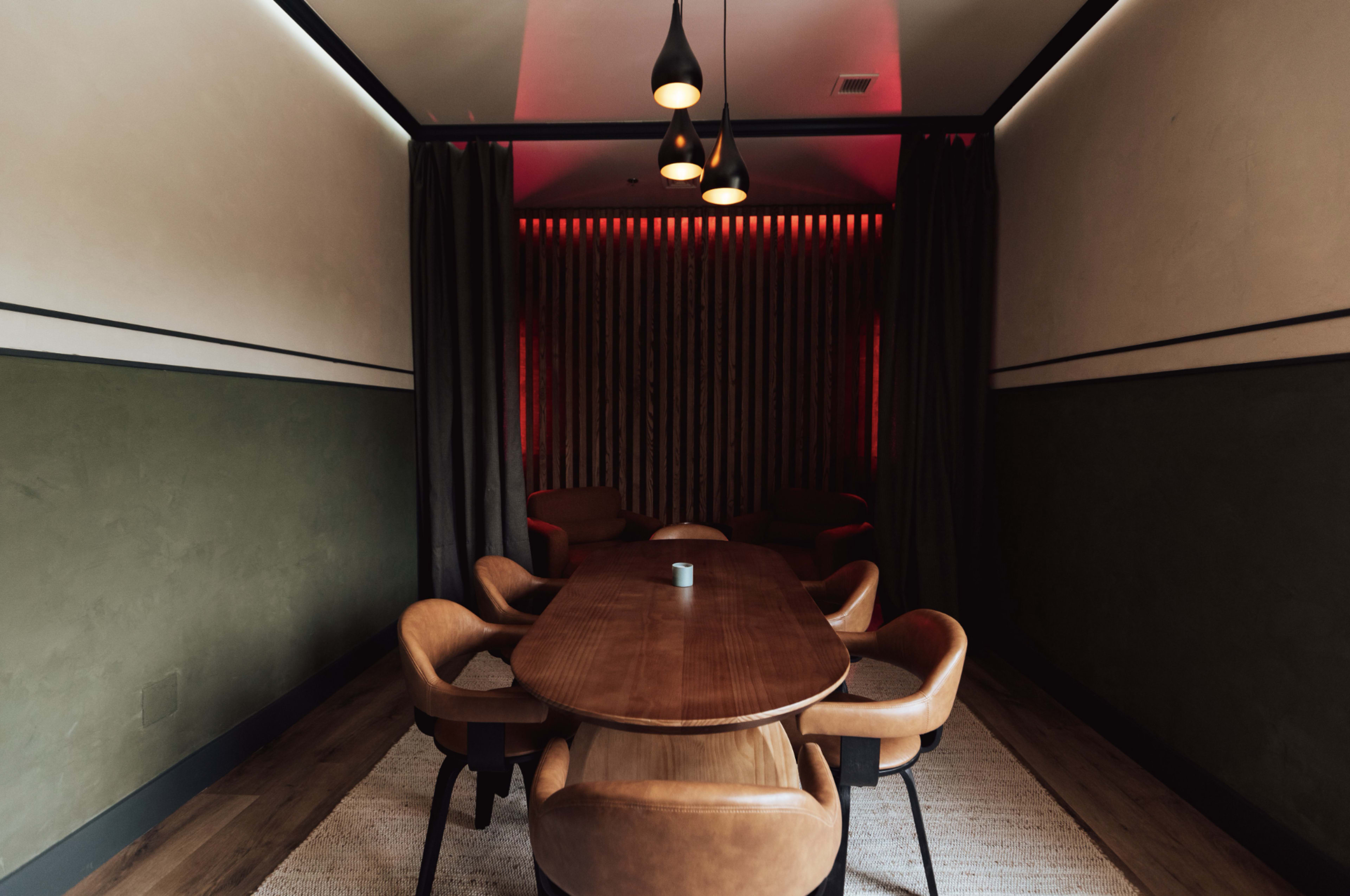 A dimly lit meeting room featuring a wooden table surrounded by modern chairs, with curtains and wall lighting creating a cozy atmosphere.
