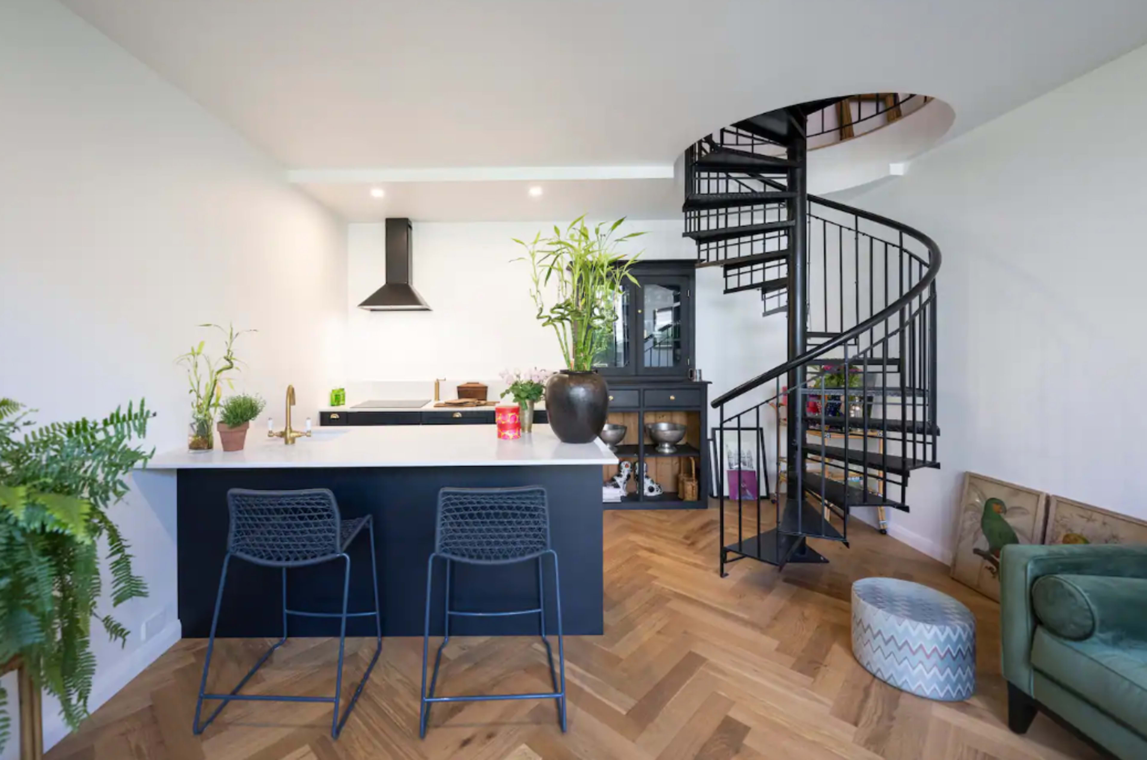 A modern kitchen and dining area featuring a spiral staircase, bar stools, and various plants.