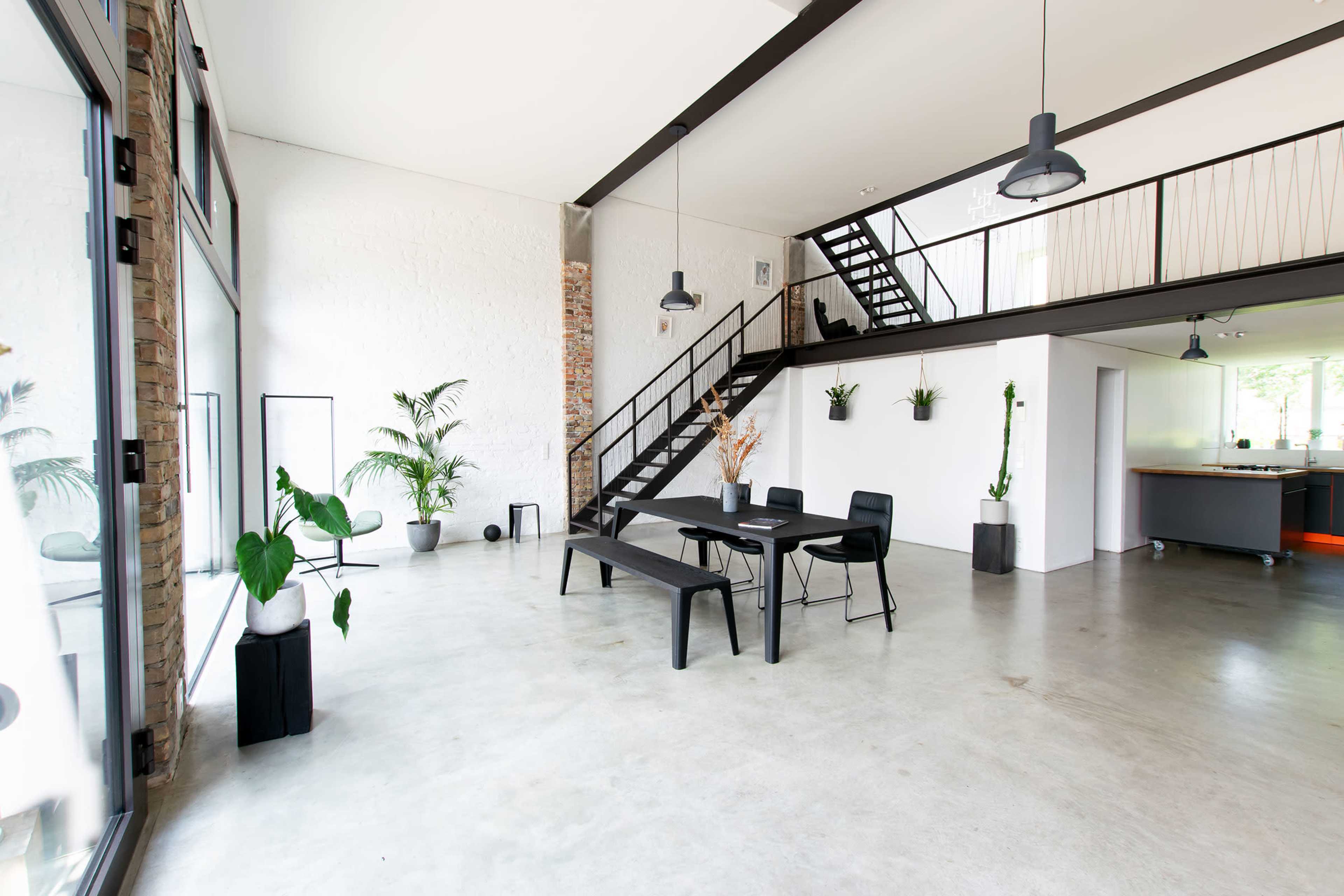 A modern interior space with a dining table and chairs, a staircase leading to an upper level, and various indoor plants placed around the room.