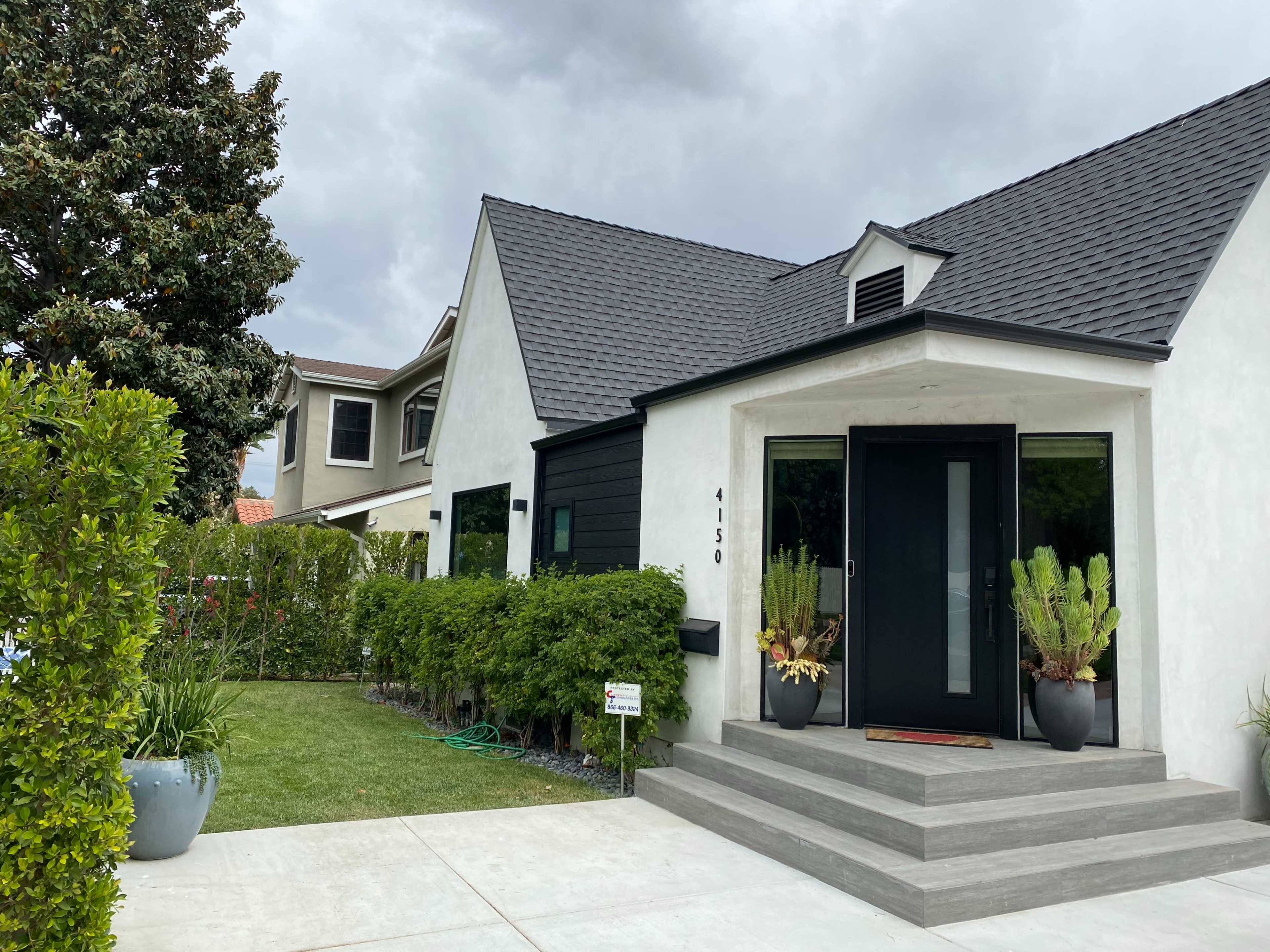 A modern house features a black and white exterior with a small front garden and a concrete walkway leading to the entrance.